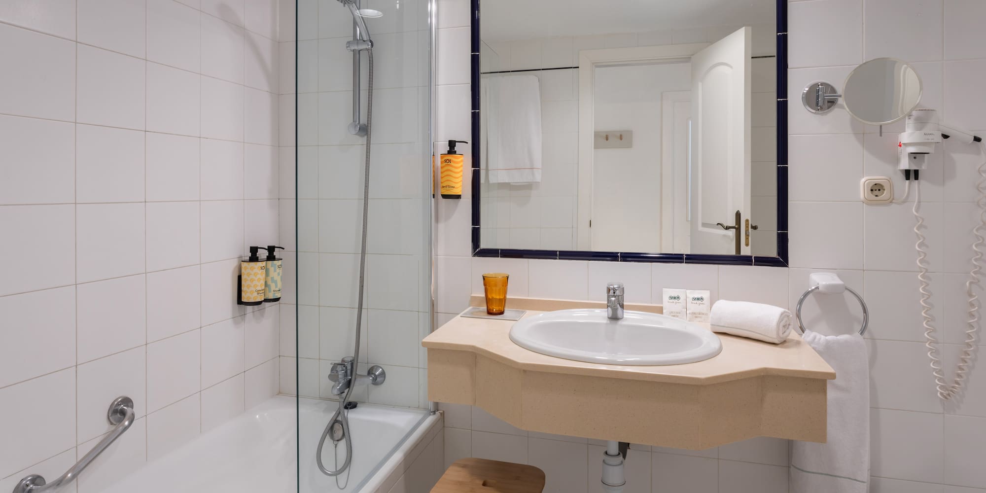 White tiled hotel bathroom with bathtub, shower, vanity sink, and mirror.