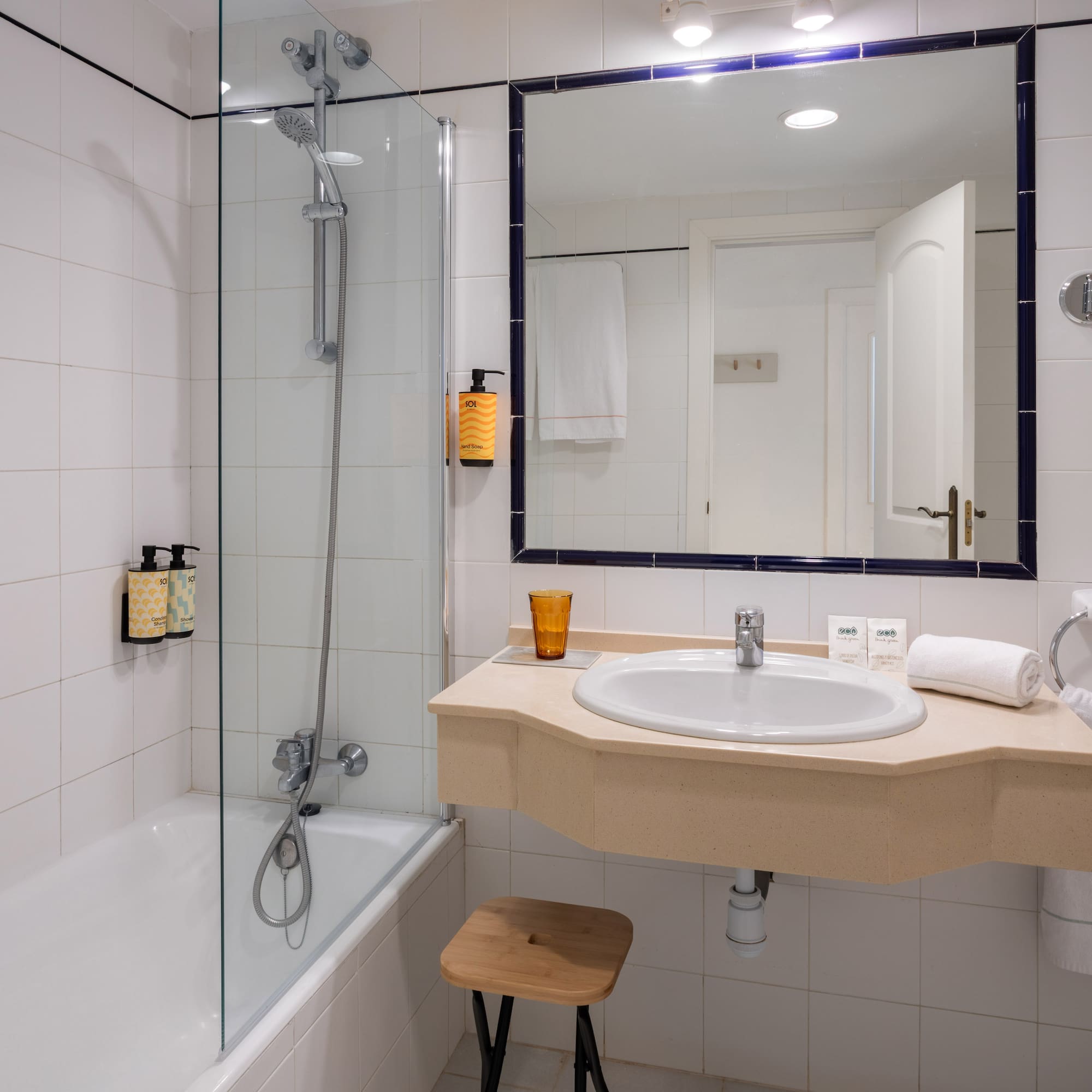 White tiled hotel bathroom with bathtub, shower, vanity sink, and mirror.