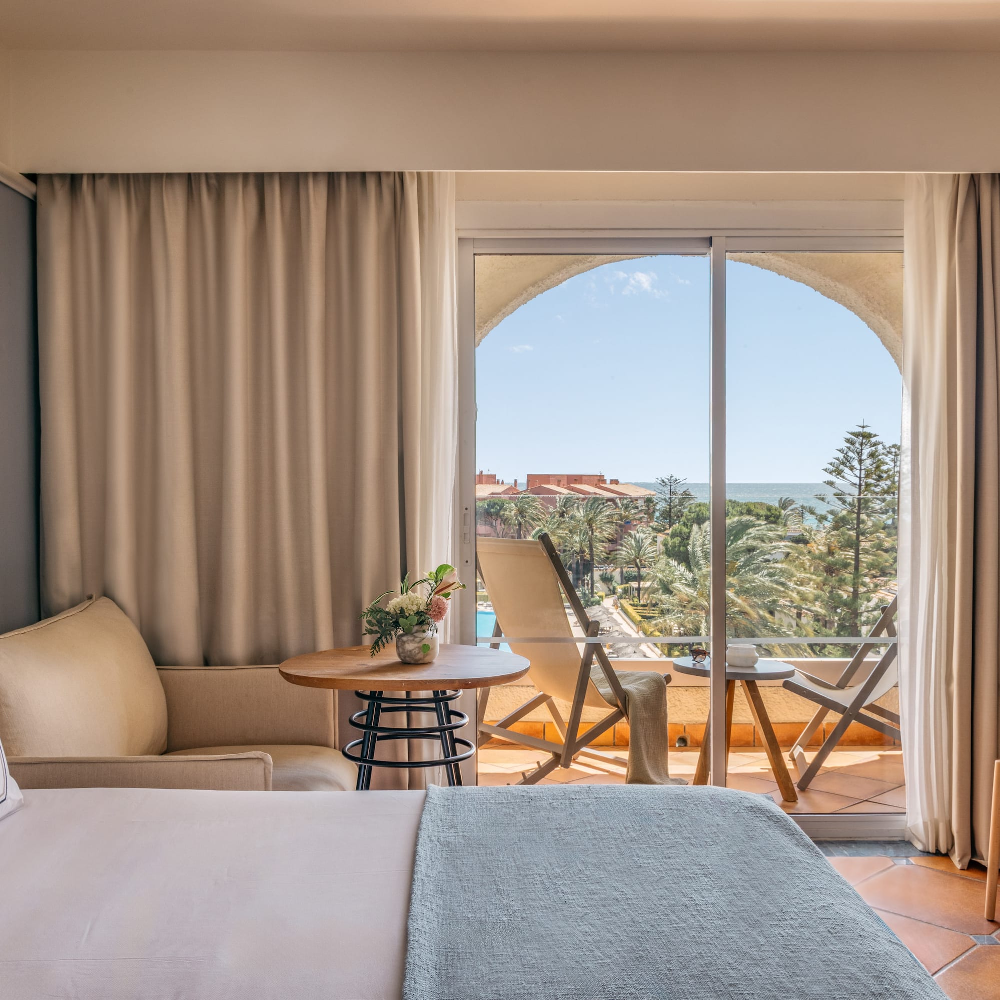 Bright hotel room with bed, balcony, and expansive sea view over a resort.