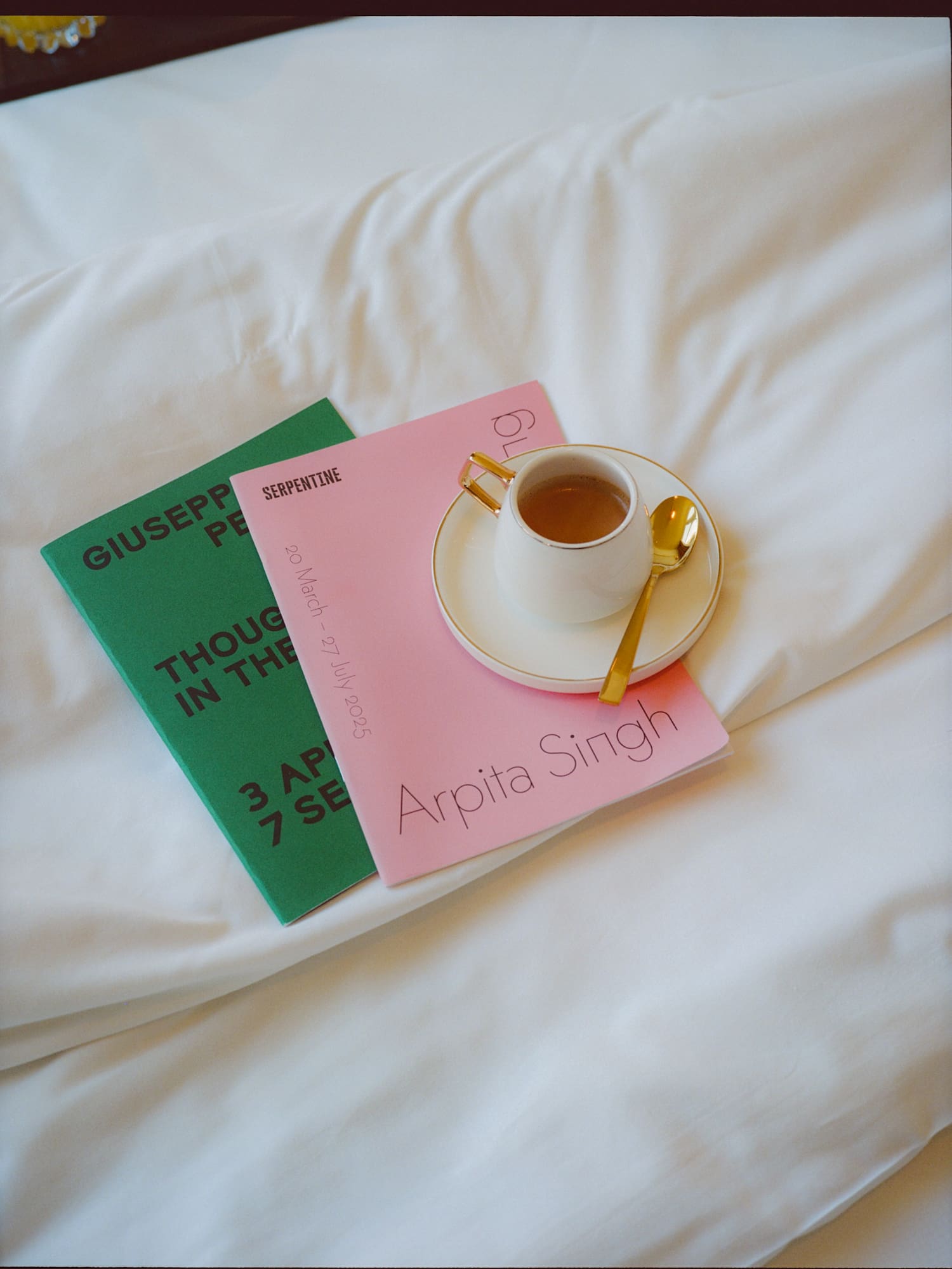 White coffee cup on pink Arpita Singh and green Serpentine exhibition books.