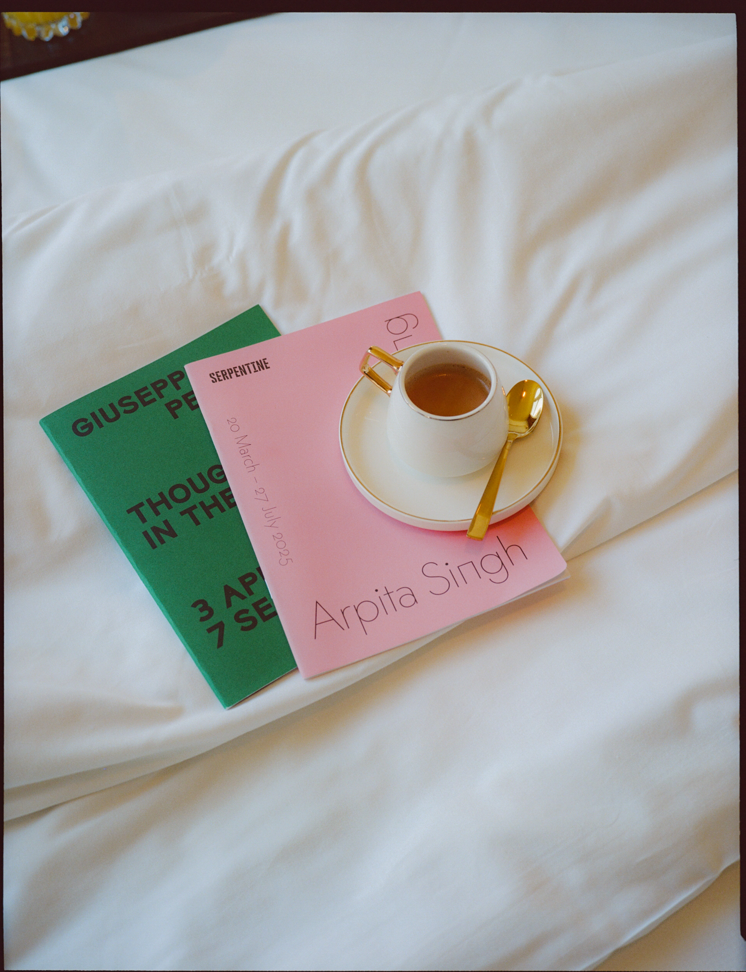 White coffee cup on pink Arpita Singh and green Serpentine exhibition books.