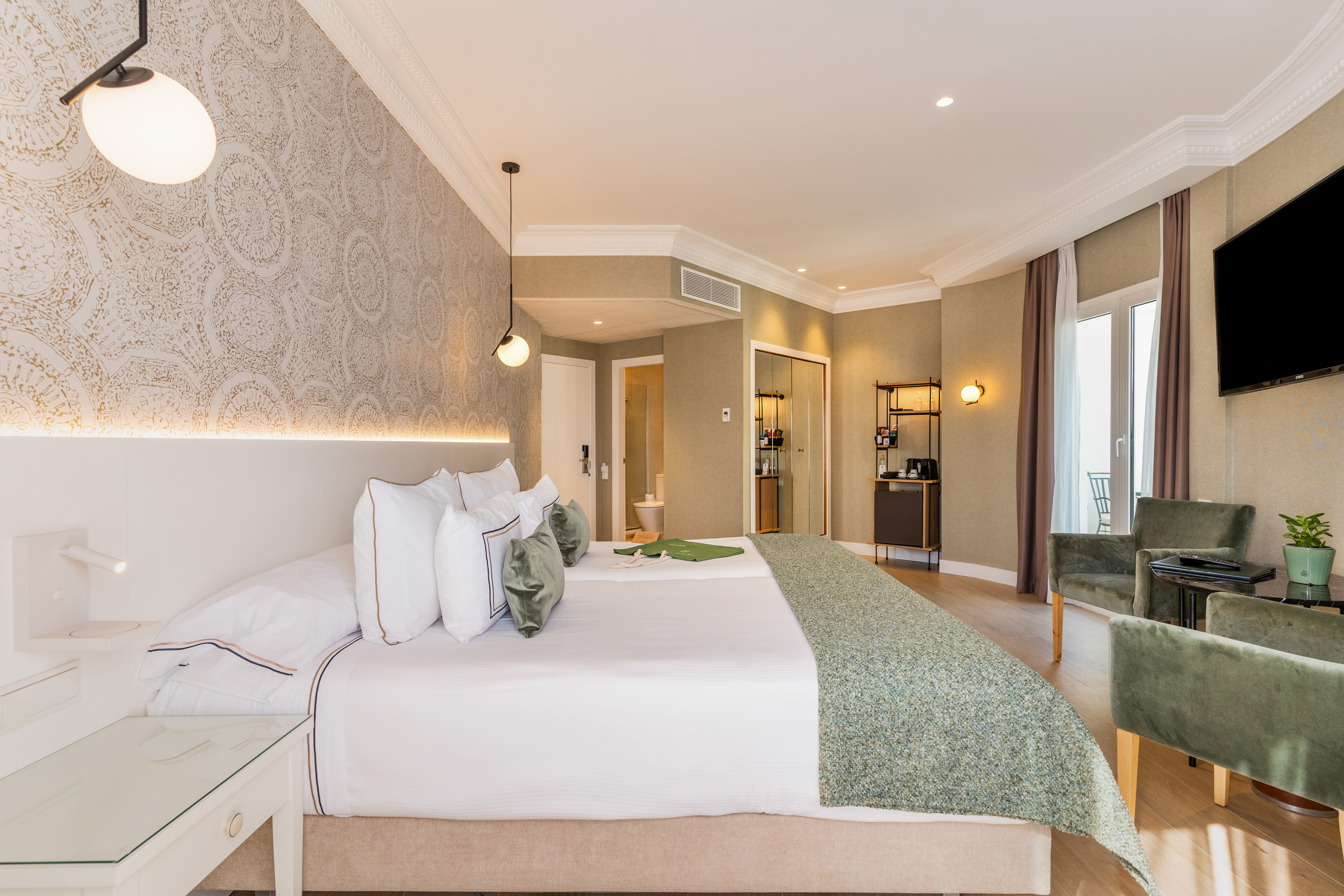 Luxury hotel room with large bed, green accents, minibar, and elegant decor.