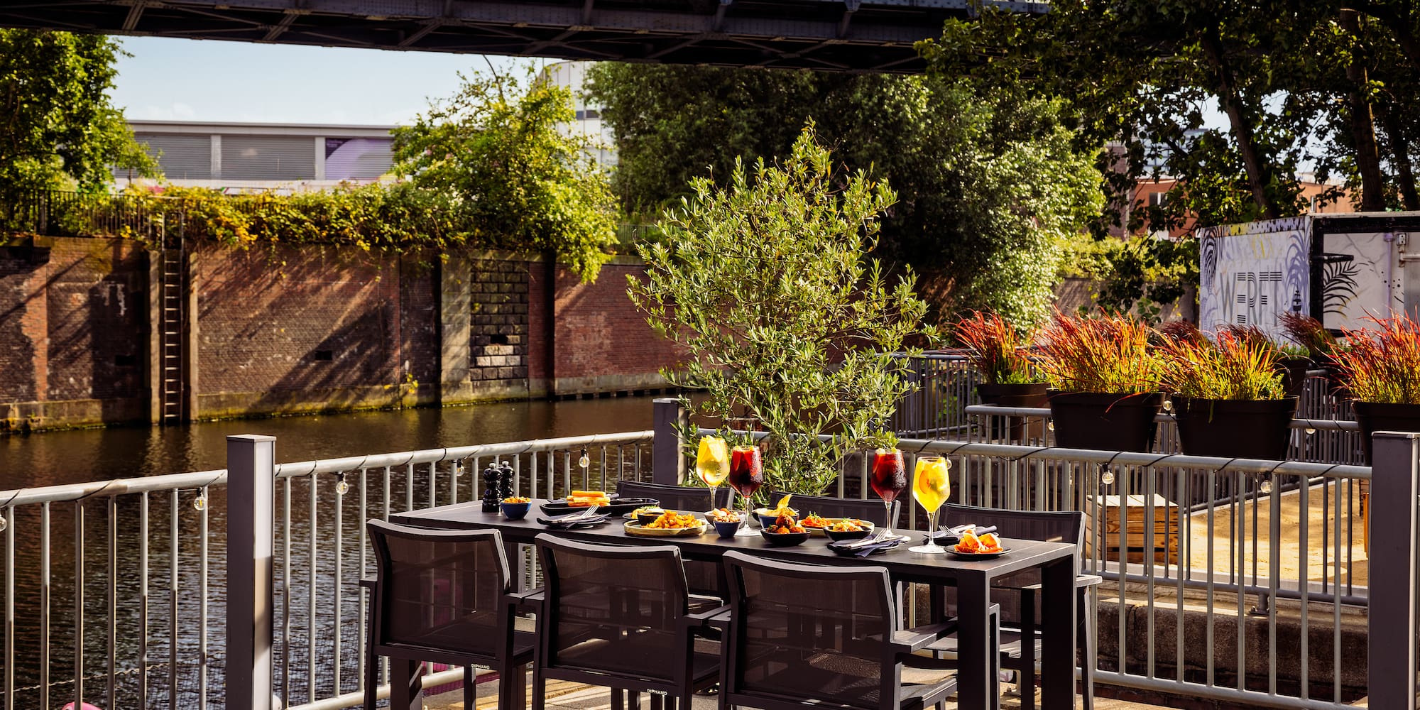 Restaurant patio with meal and drinks next to a canal and bridge.