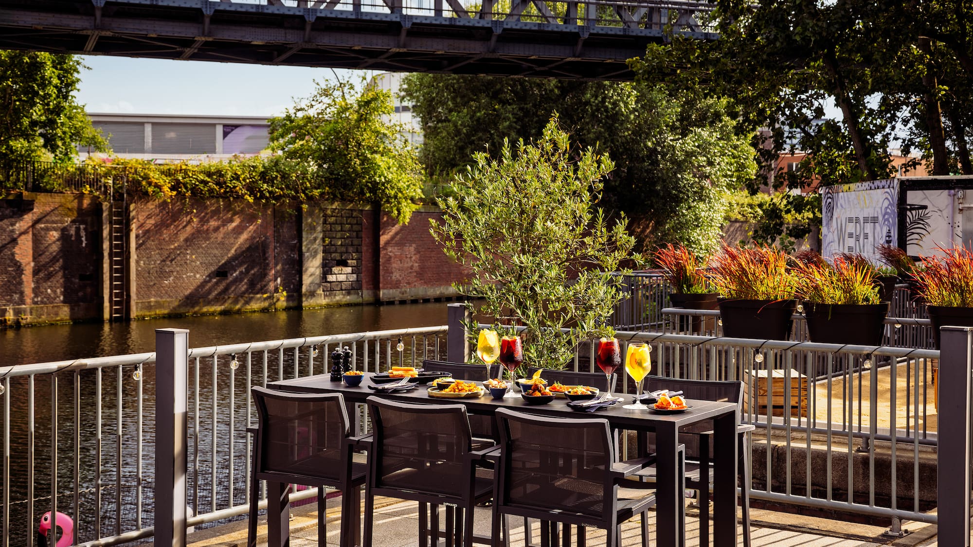 Restaurant patio with meal and drinks next to a canal and bridge.