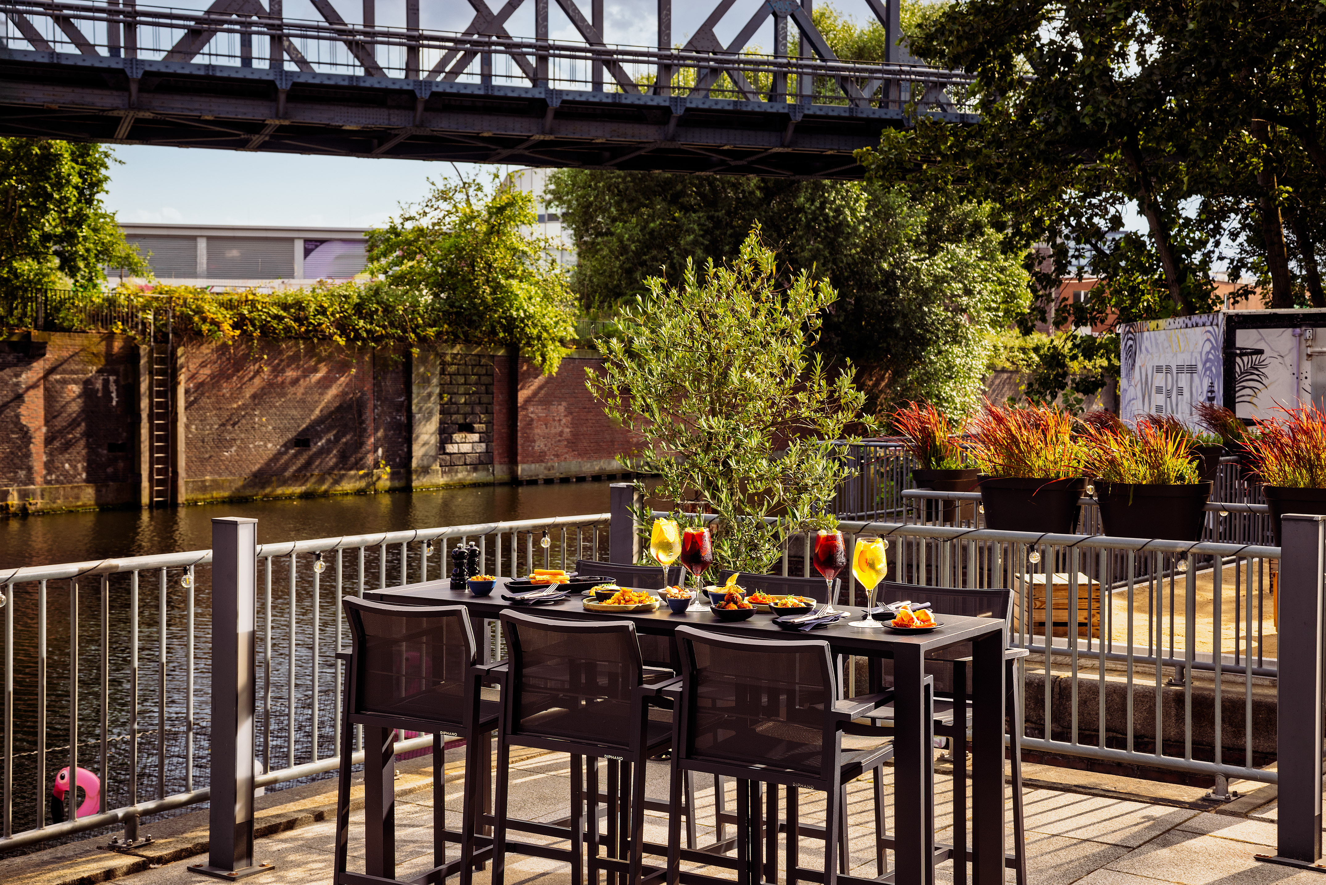 Restaurant patio with meal and drinks next to a canal and bridge.
