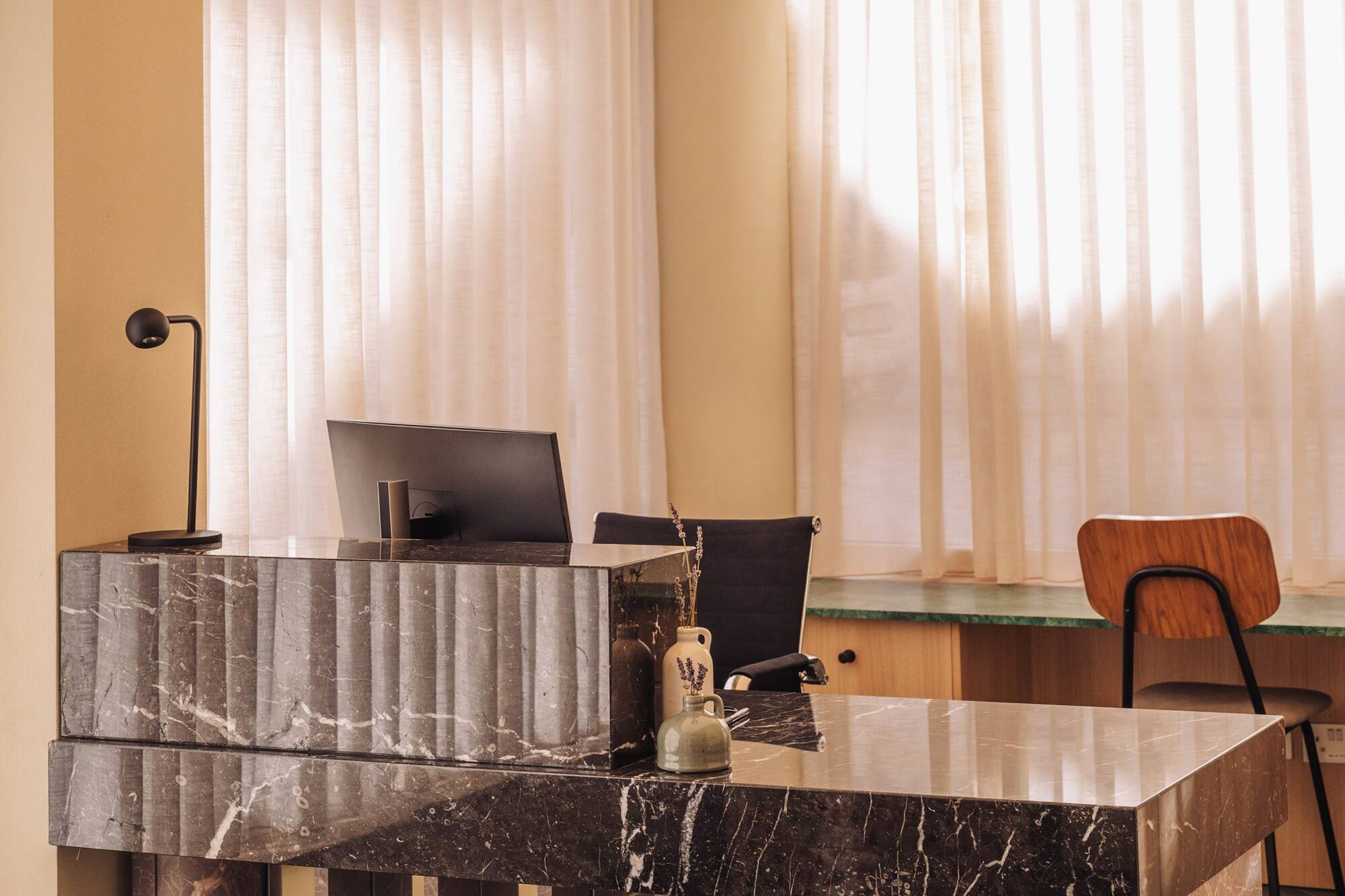 Elegant dark marble reception desk with monitor in a sunlit modern office.