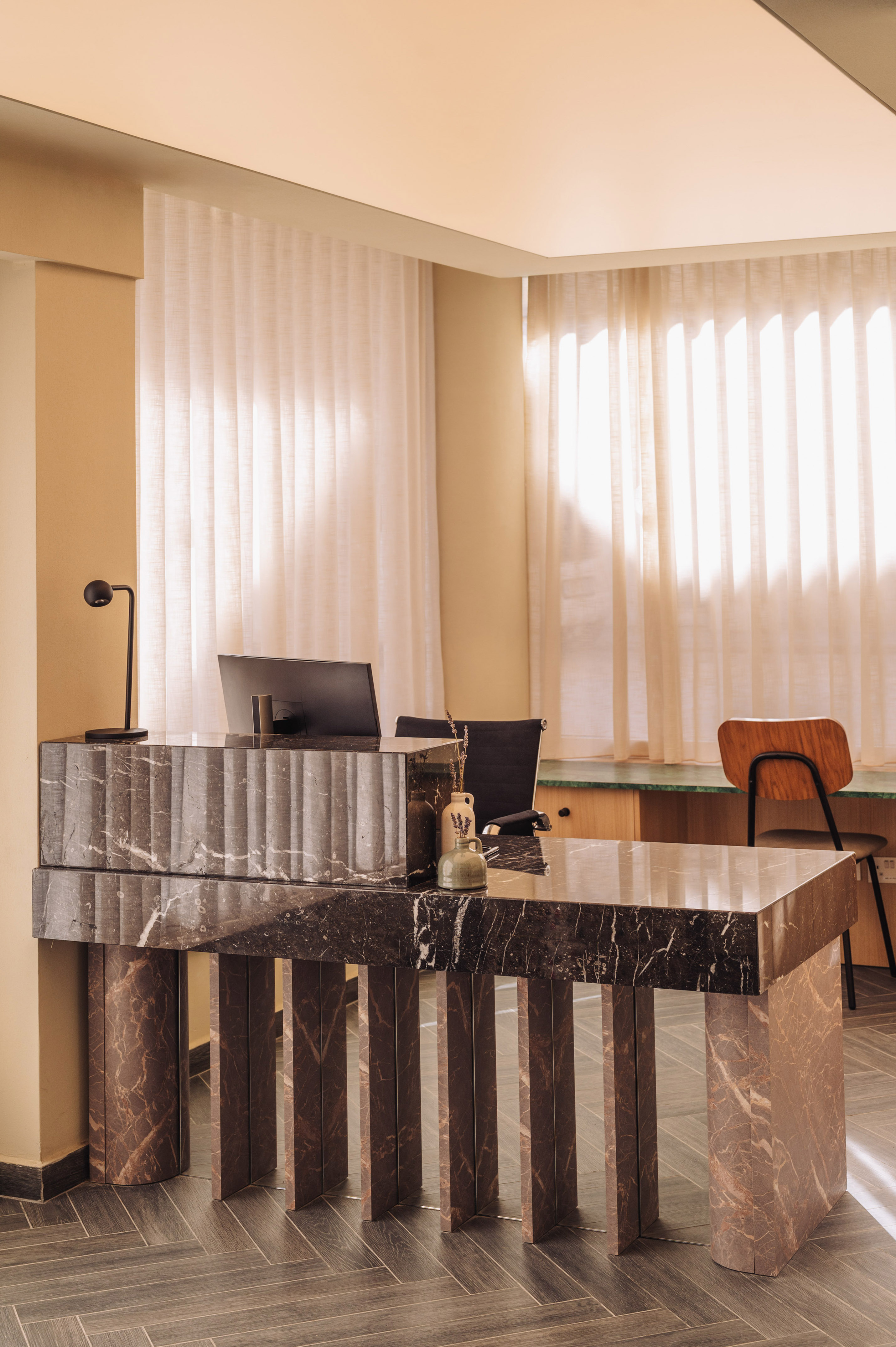 Elegant dark marble reception desk with monitor in a sunlit modern office.
