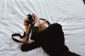 a woman lying on a bed holding a camera