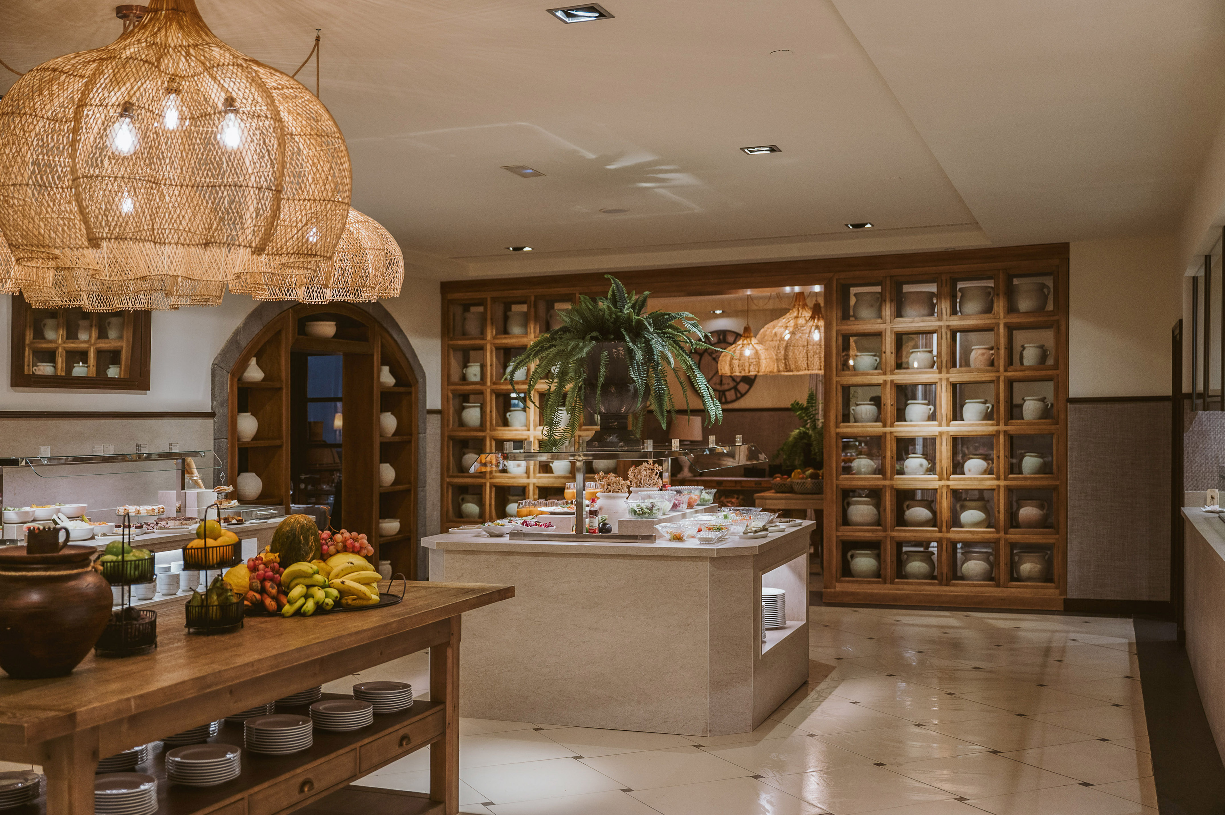 Hotel buffet with fresh fruit, food displays, and decorative wicker pendant lights.