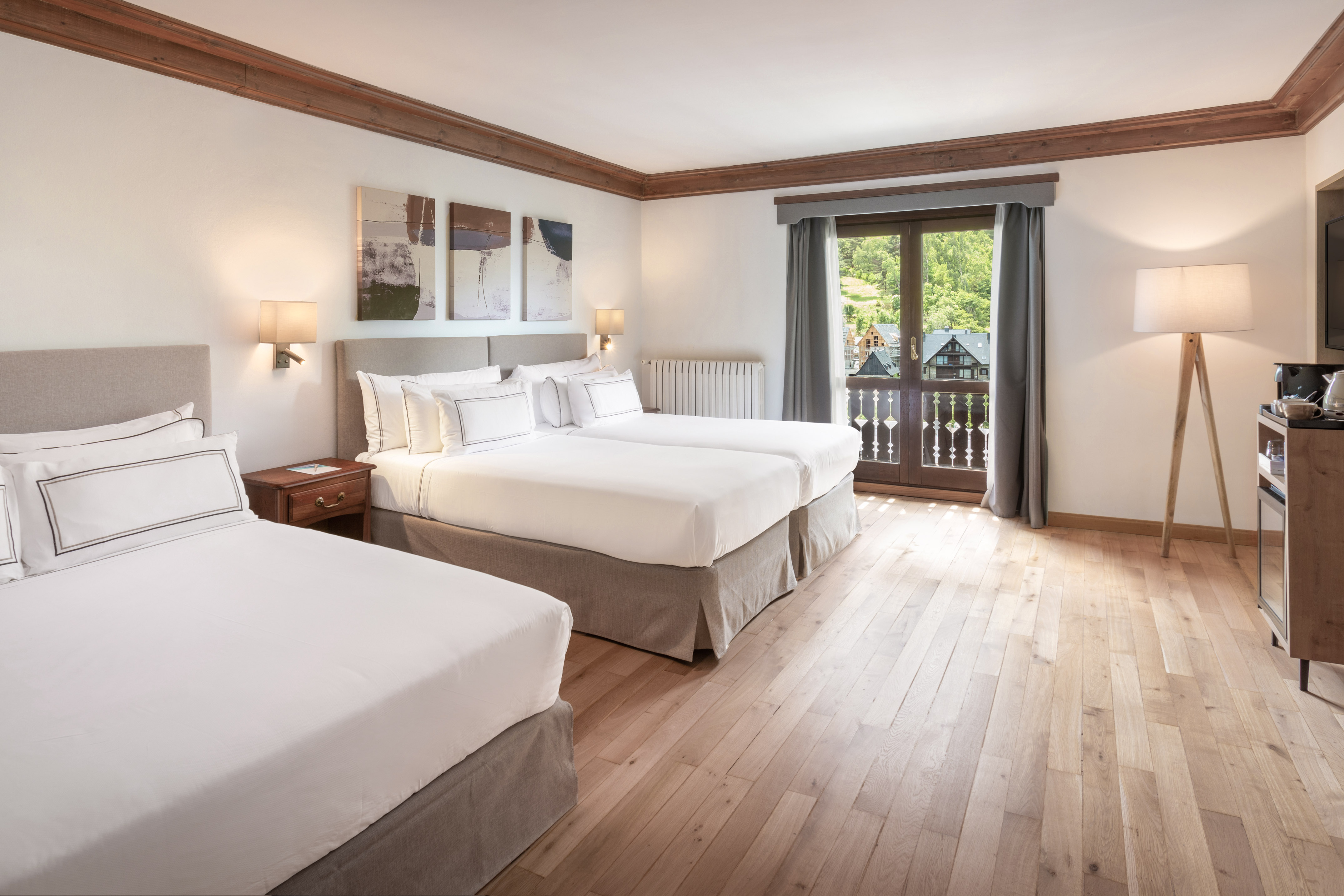 Spacious hotel room with double and twin beds, wooden floor, balcony, mountain view.