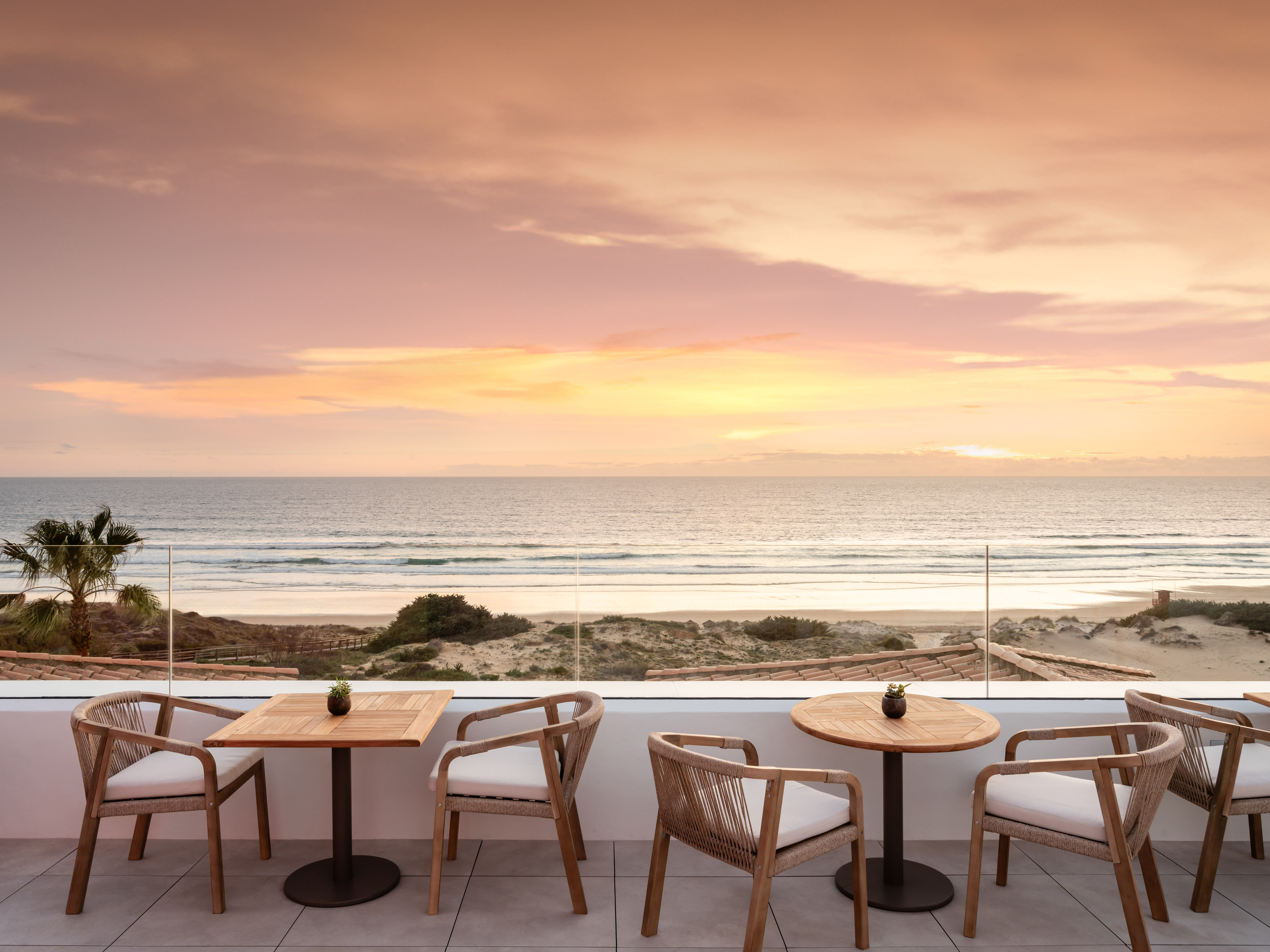 Oceanfront terrace with modern outdoor seating, sandy beach, and sunset sky.