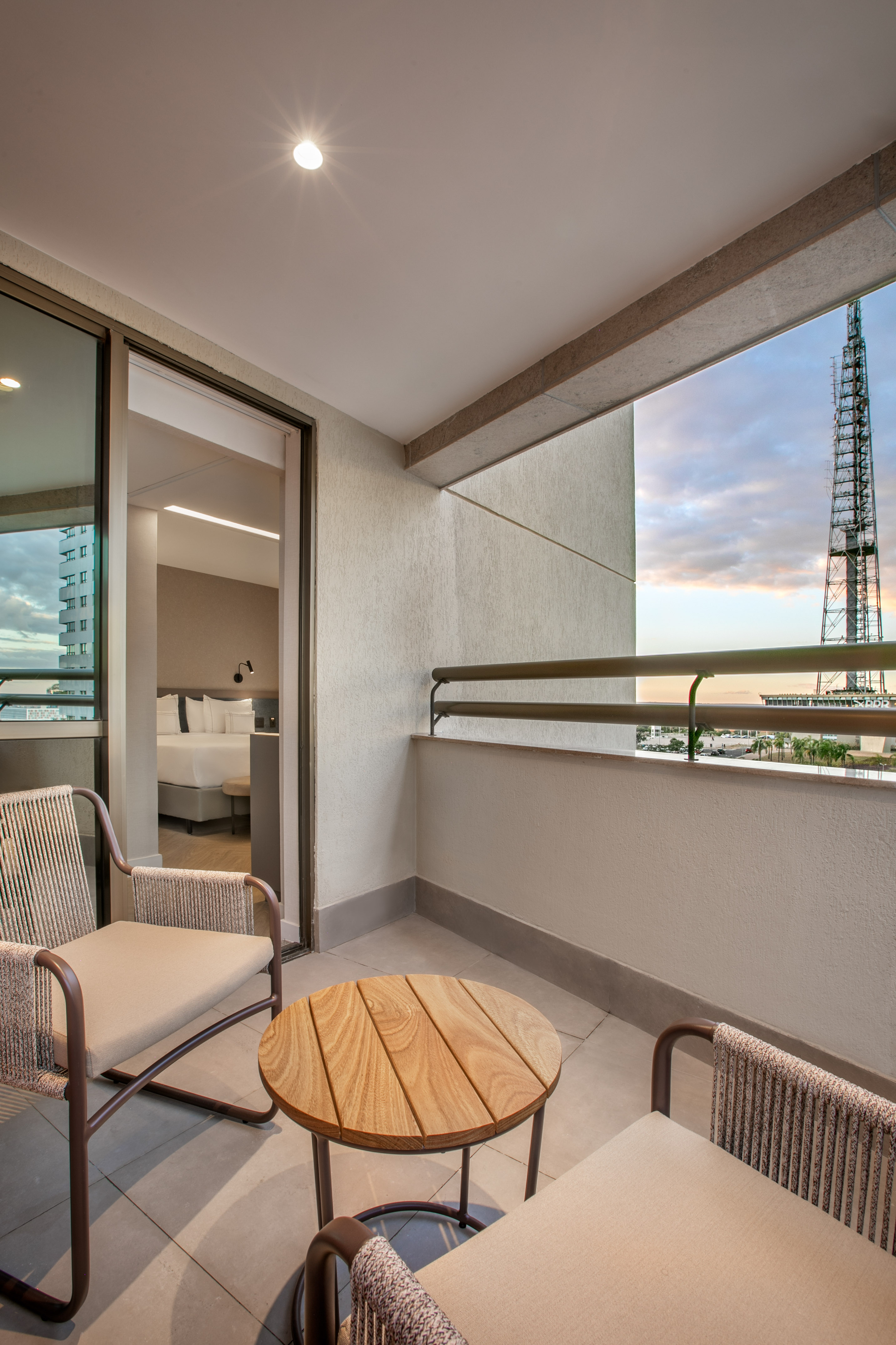 Hotel balcony with outdoor furniture, city skyline view, and modern hotel room.