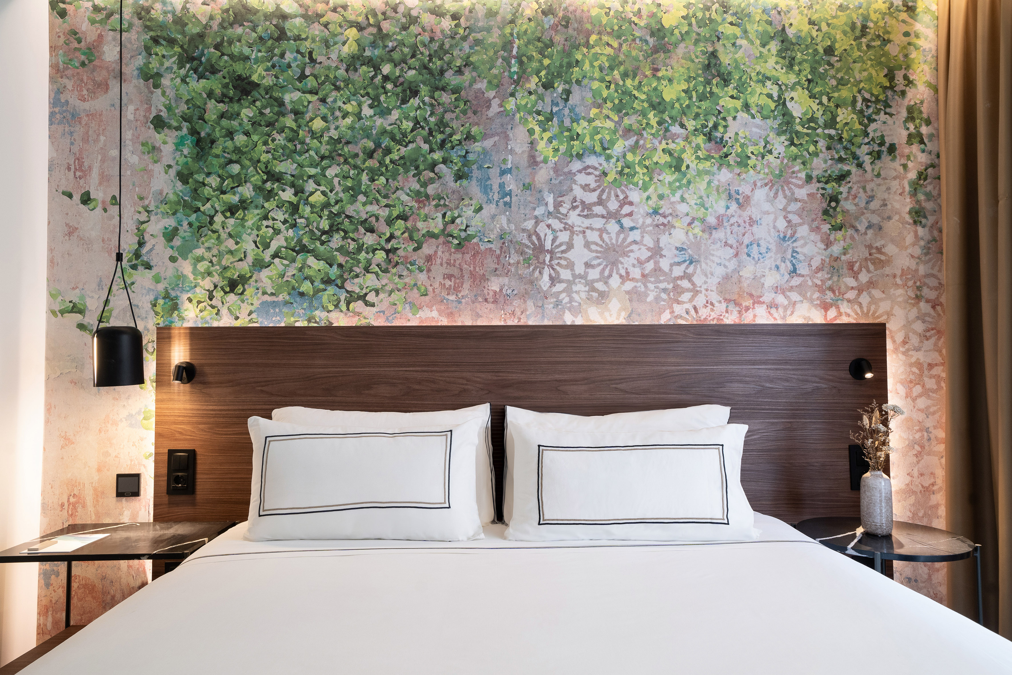 Hotel bedroom with white bed, dark wood headboard, and green leaf wall mural.