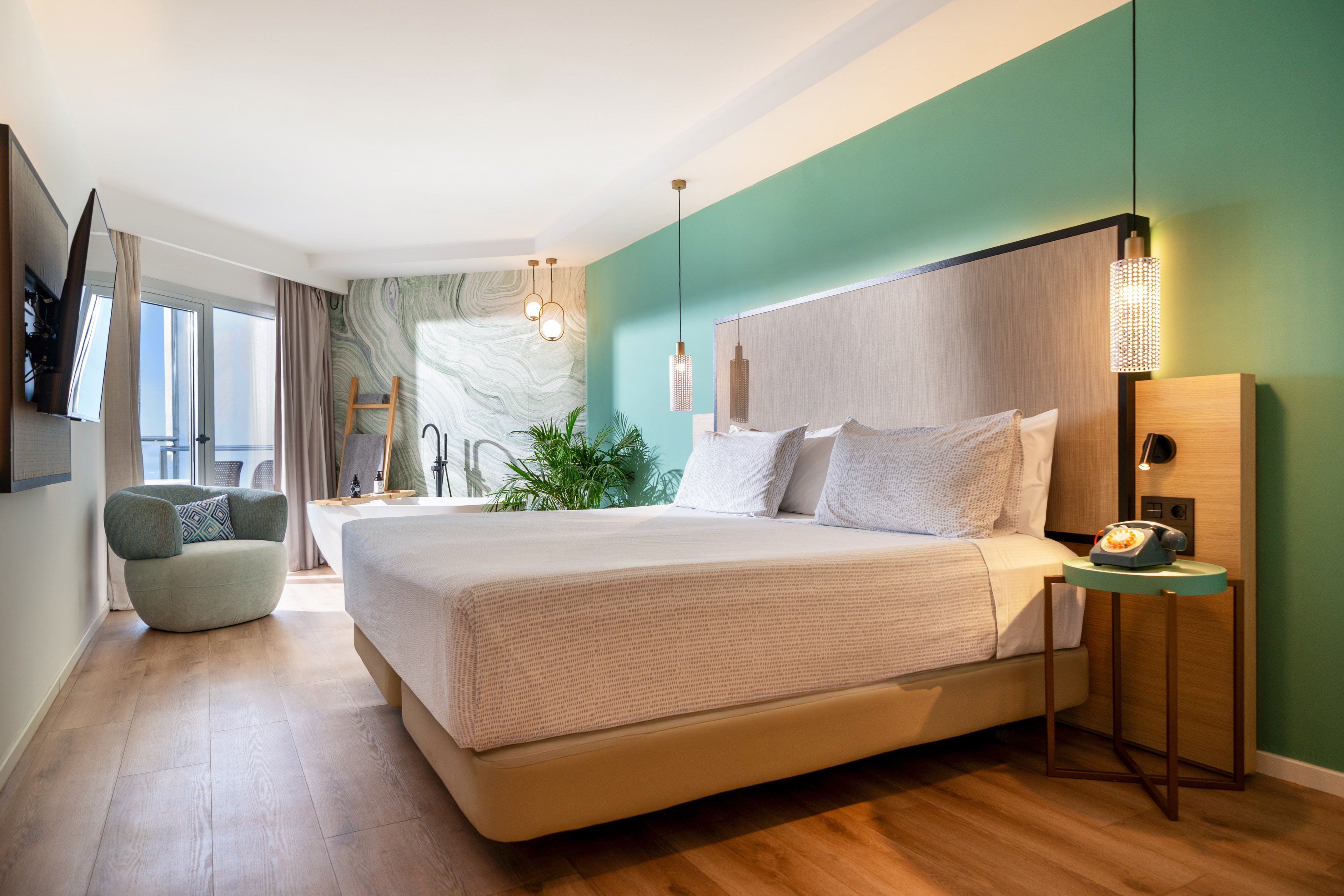 Modern hotel room: king bed, green wall, freestanding tub, balcony.
