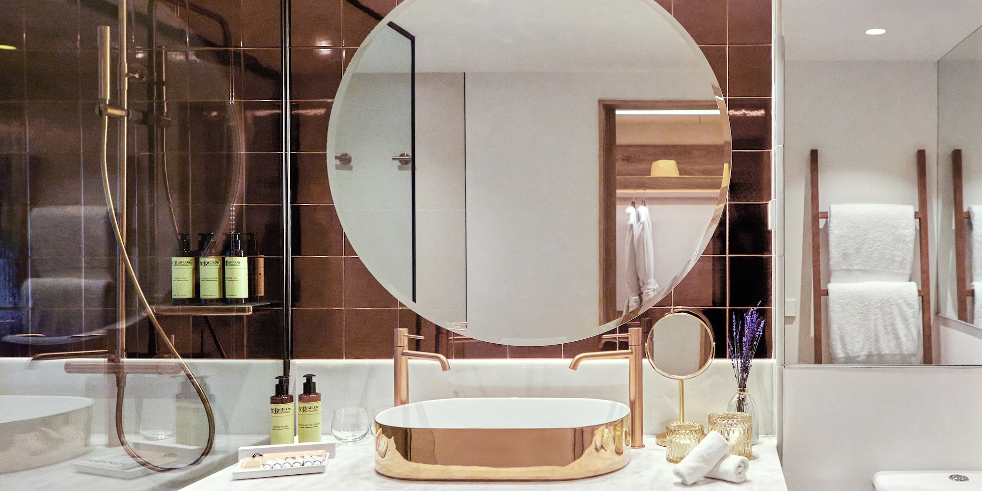 Luxury modern bathroom with gold sink, round mirror, marble vanity, and bronze tiles.