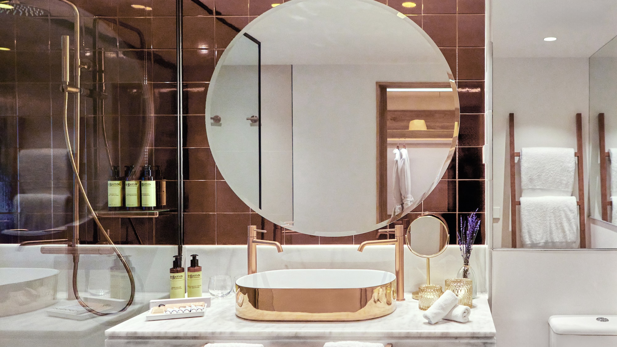 Luxury modern bathroom with gold sink, round mirror, marble vanity, and bronze tiles.