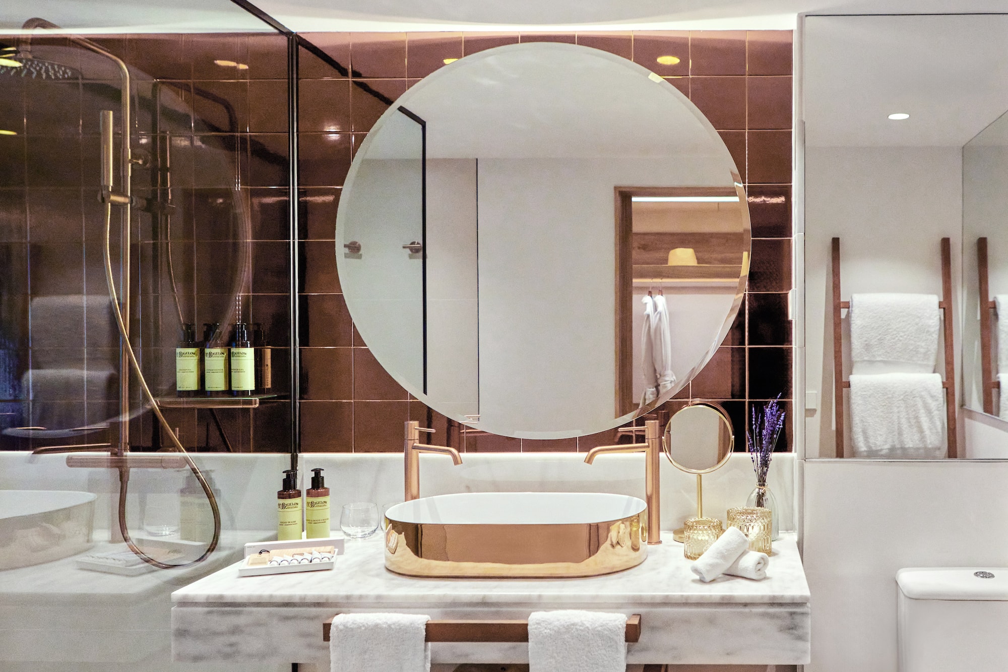 Luxury modern bathroom with gold sink, round mirror, marble vanity, and bronze tiles.