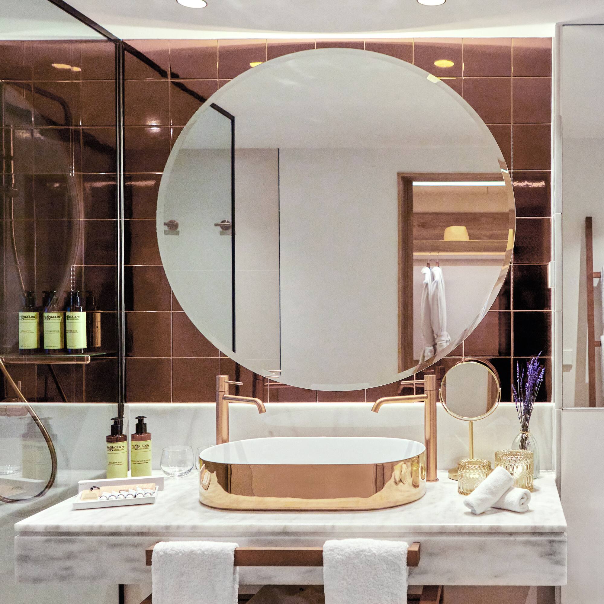 Luxury modern bathroom with gold sink, round mirror, marble vanity, and bronze tiles.