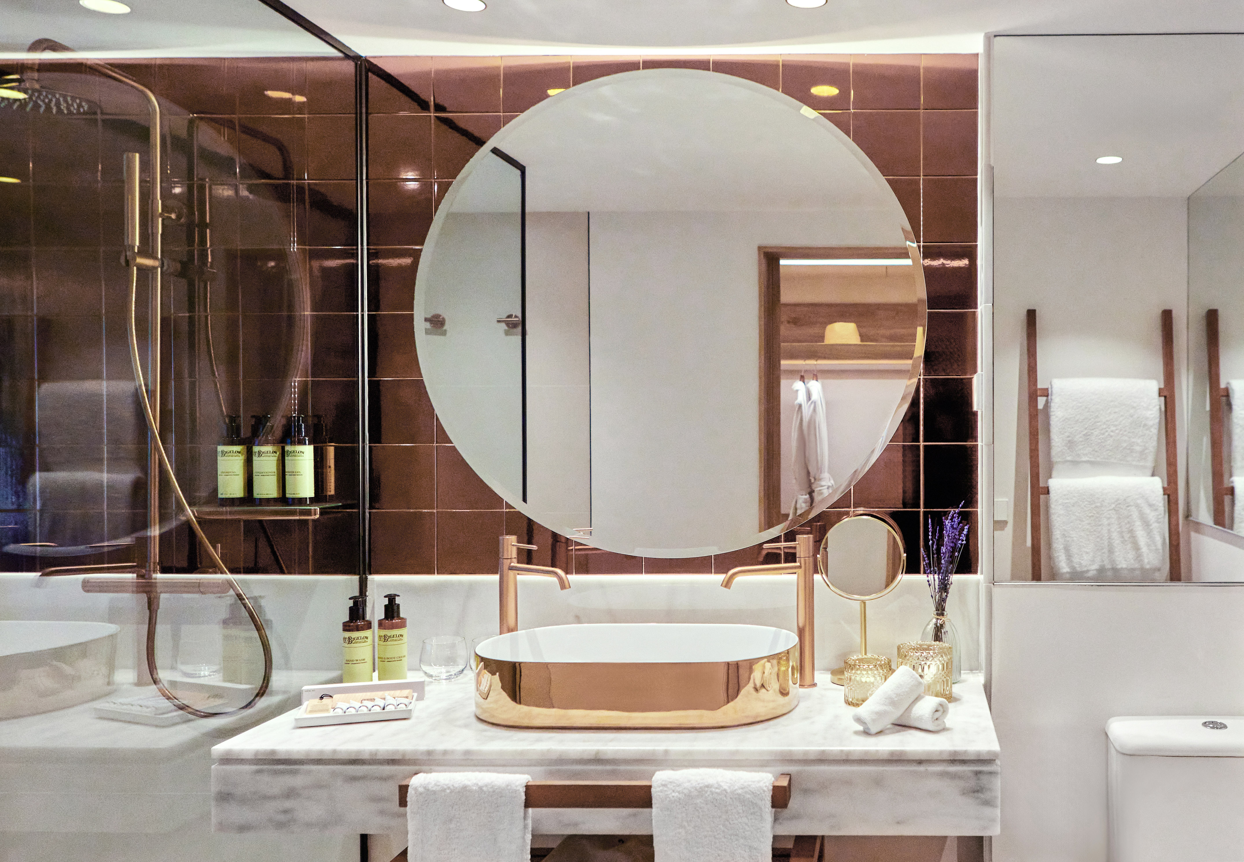 Luxury modern bathroom with gold sink, round mirror, marble vanity, and bronze tiles.