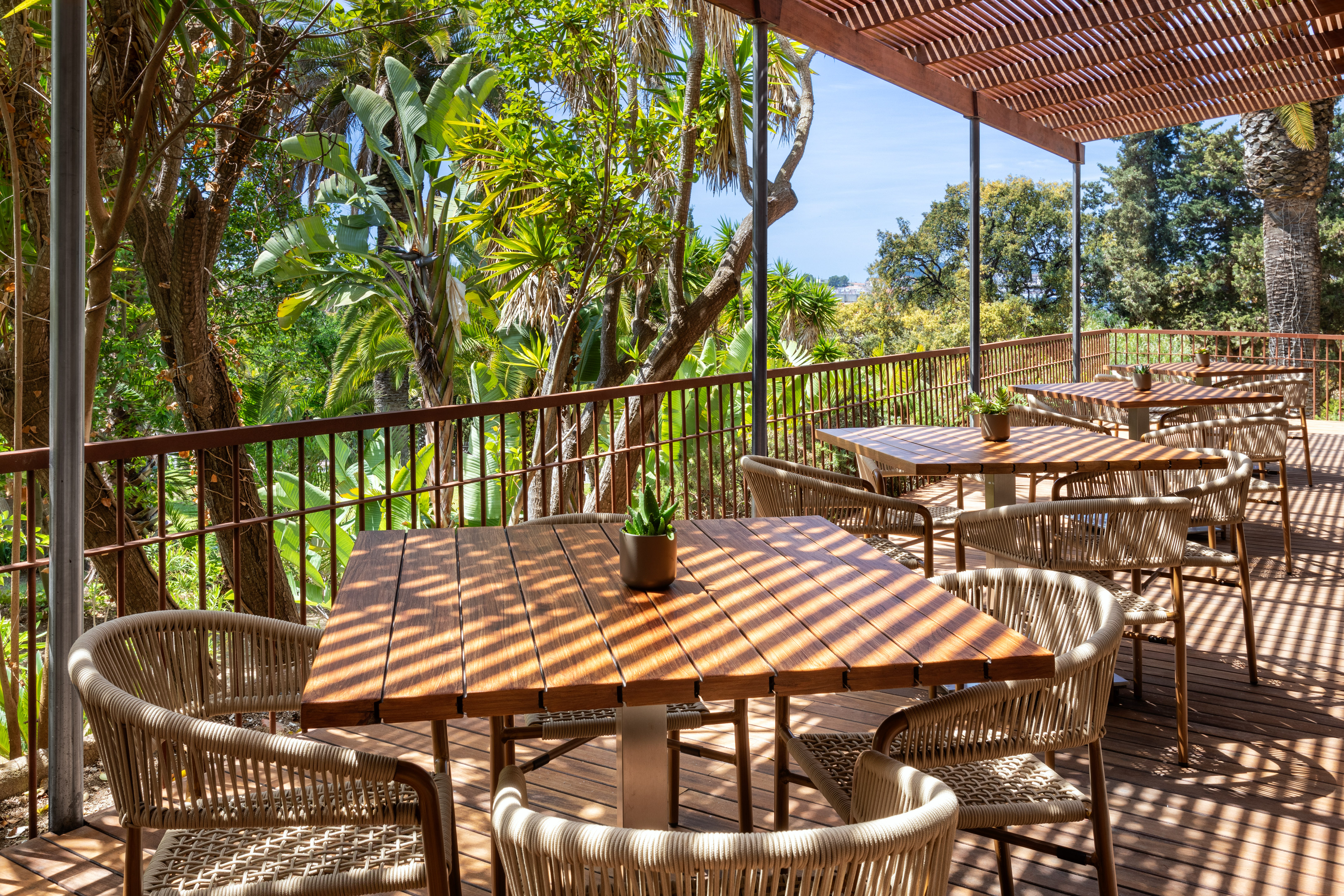 Outdoor tropical restaurant patio with shaded wooden tables and woven chairs.