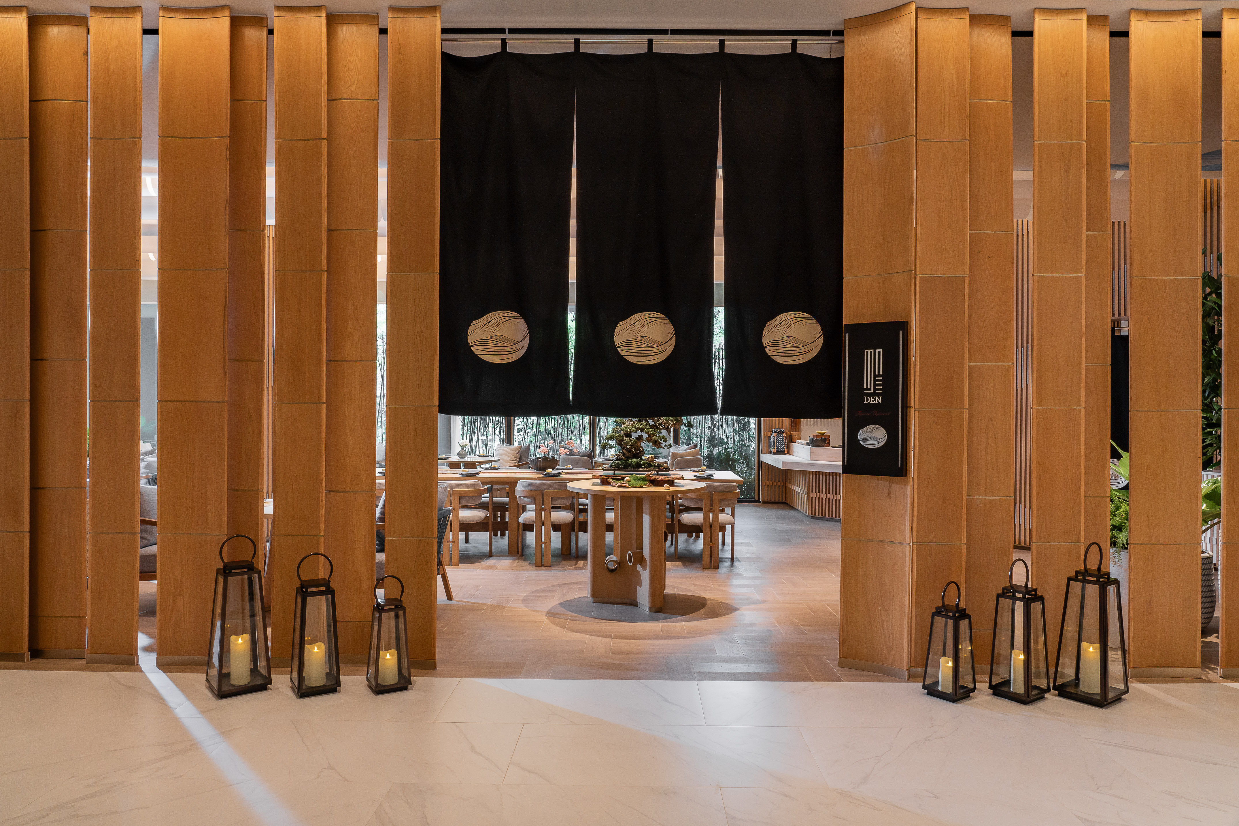 DEN Japanese restaurant entrance with Noren curtains, wood screens, dining tables.