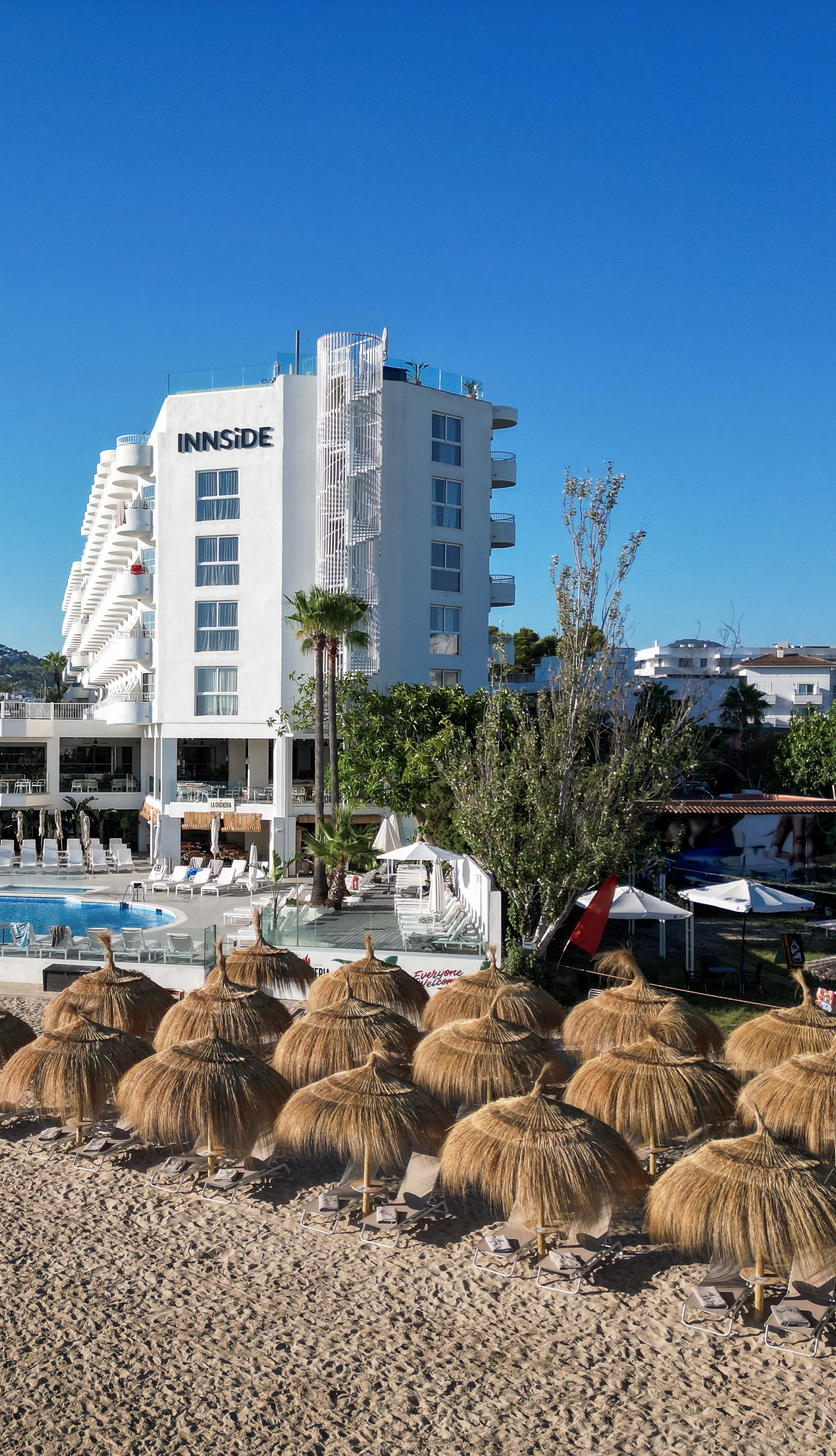 INNSiDE hotel, sandy beach with straw umbrellas, and swimming pool.