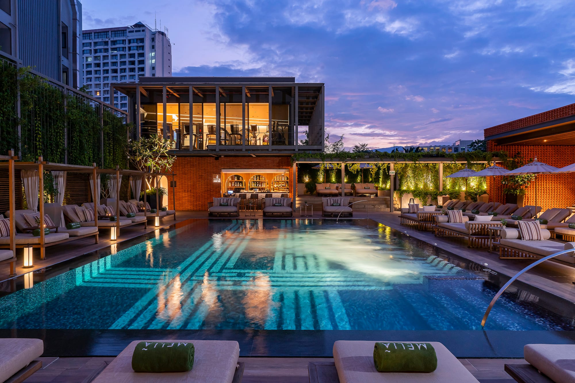 Meliá hotel pool and bar at dusk, with glowing water, lounge chairs, and city.