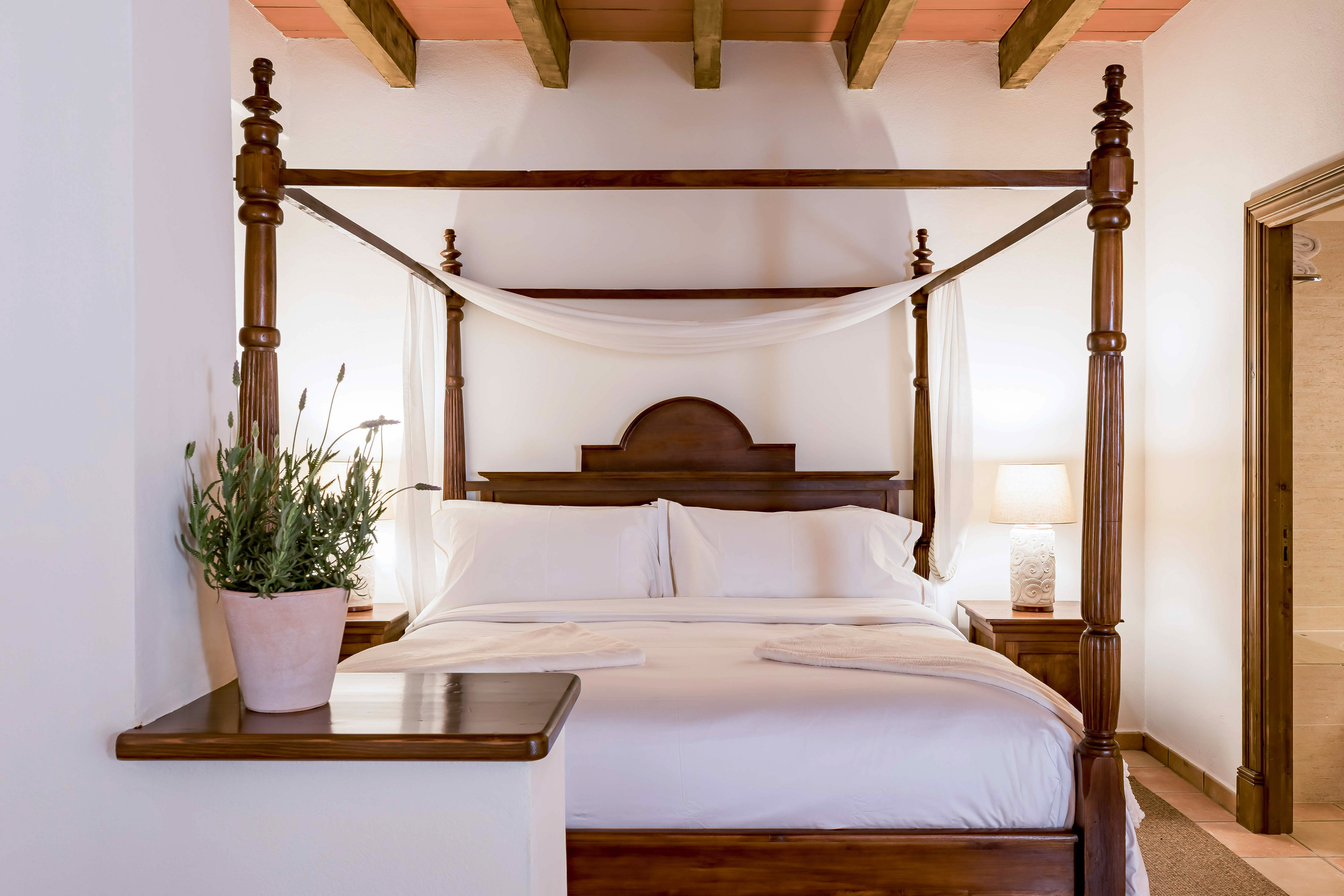 Luxurious four-poster bed with white drapes in a Mediterranean hotel room.