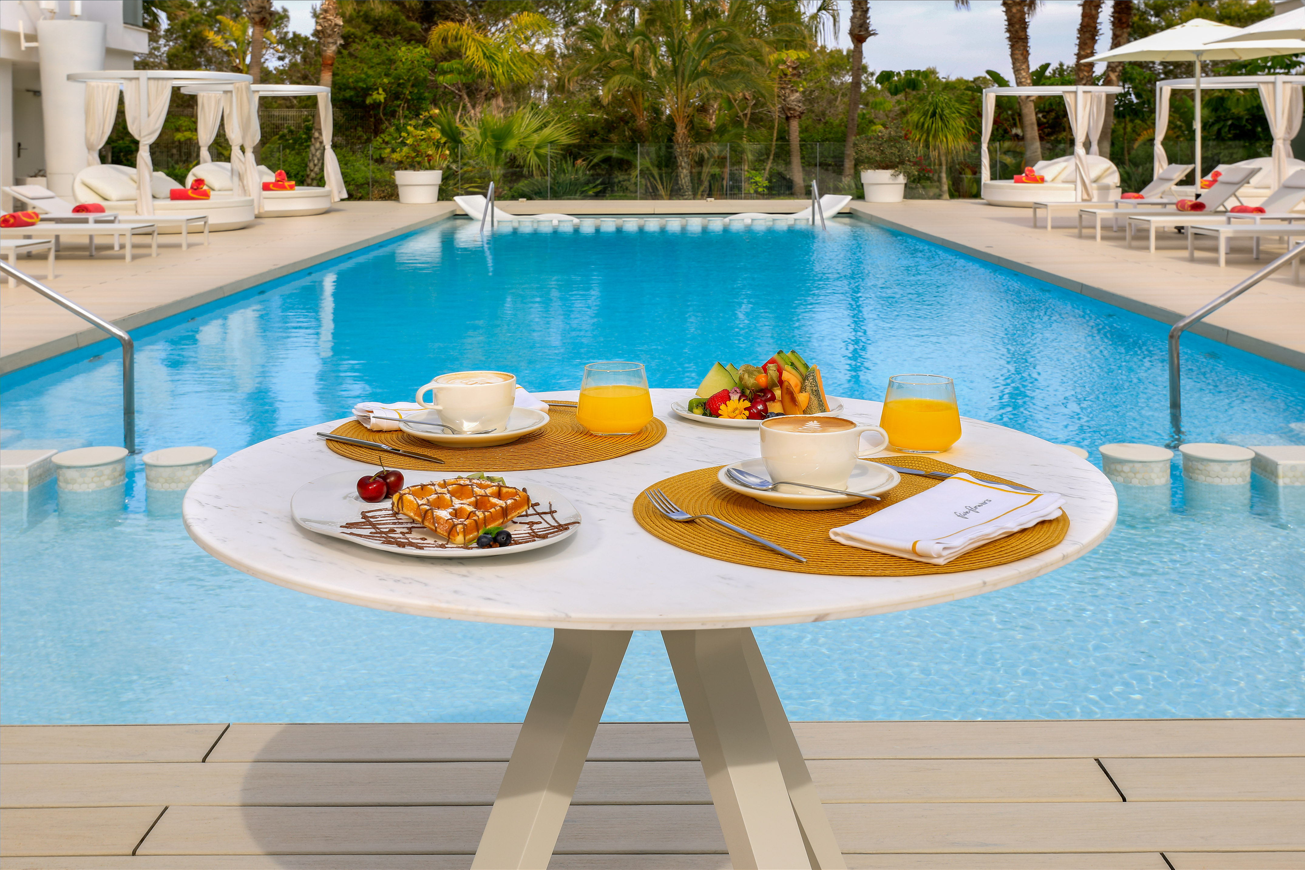 Luxury poolside breakfast: waffles, fruit, coffee, orange juice by resort pool.