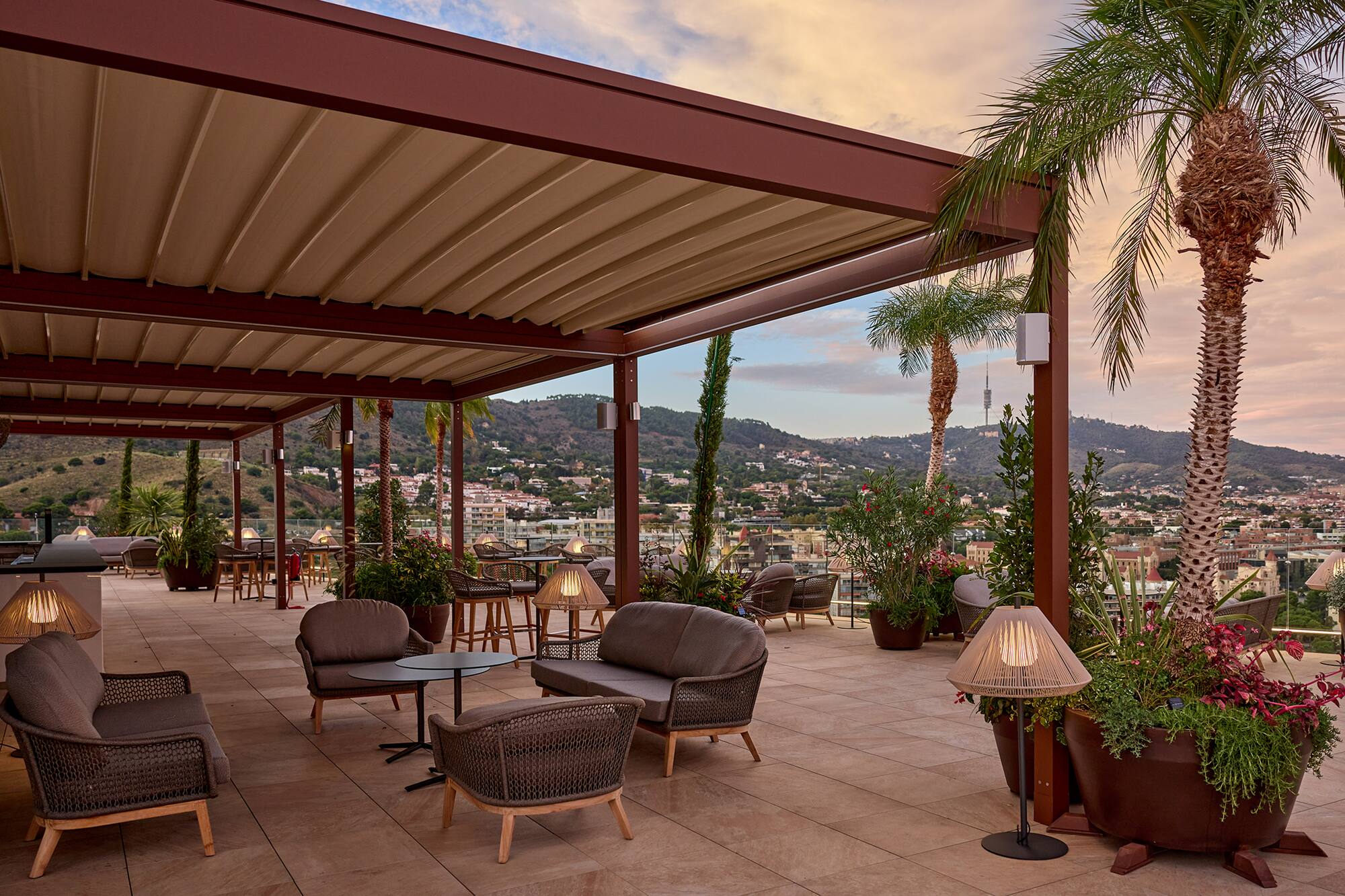 Rooftop terrace with pergola, outdoor lounge seating, palm trees, city view at dusk.