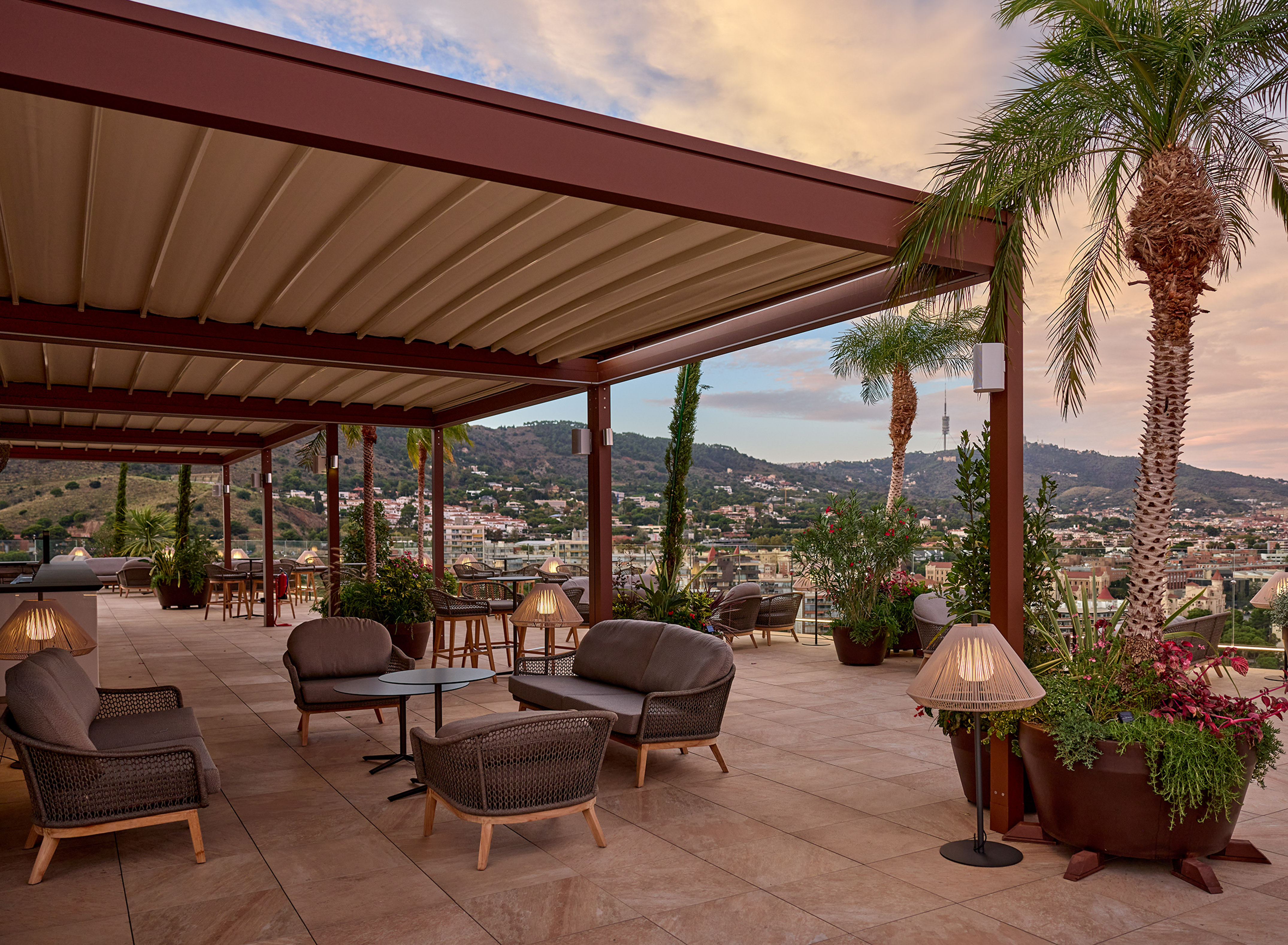 Rooftop terrace with pergola, outdoor lounge seating, palm trees, city view at dusk.