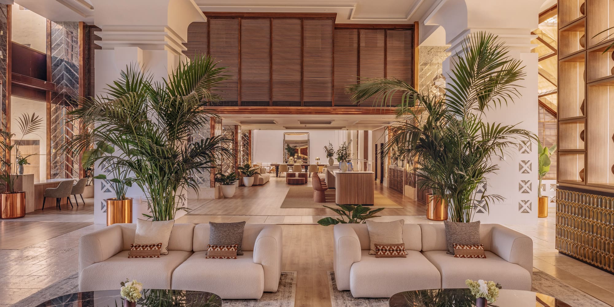 Modern hotel lobby with cream sofas, black marble tables, and lush palm plants.