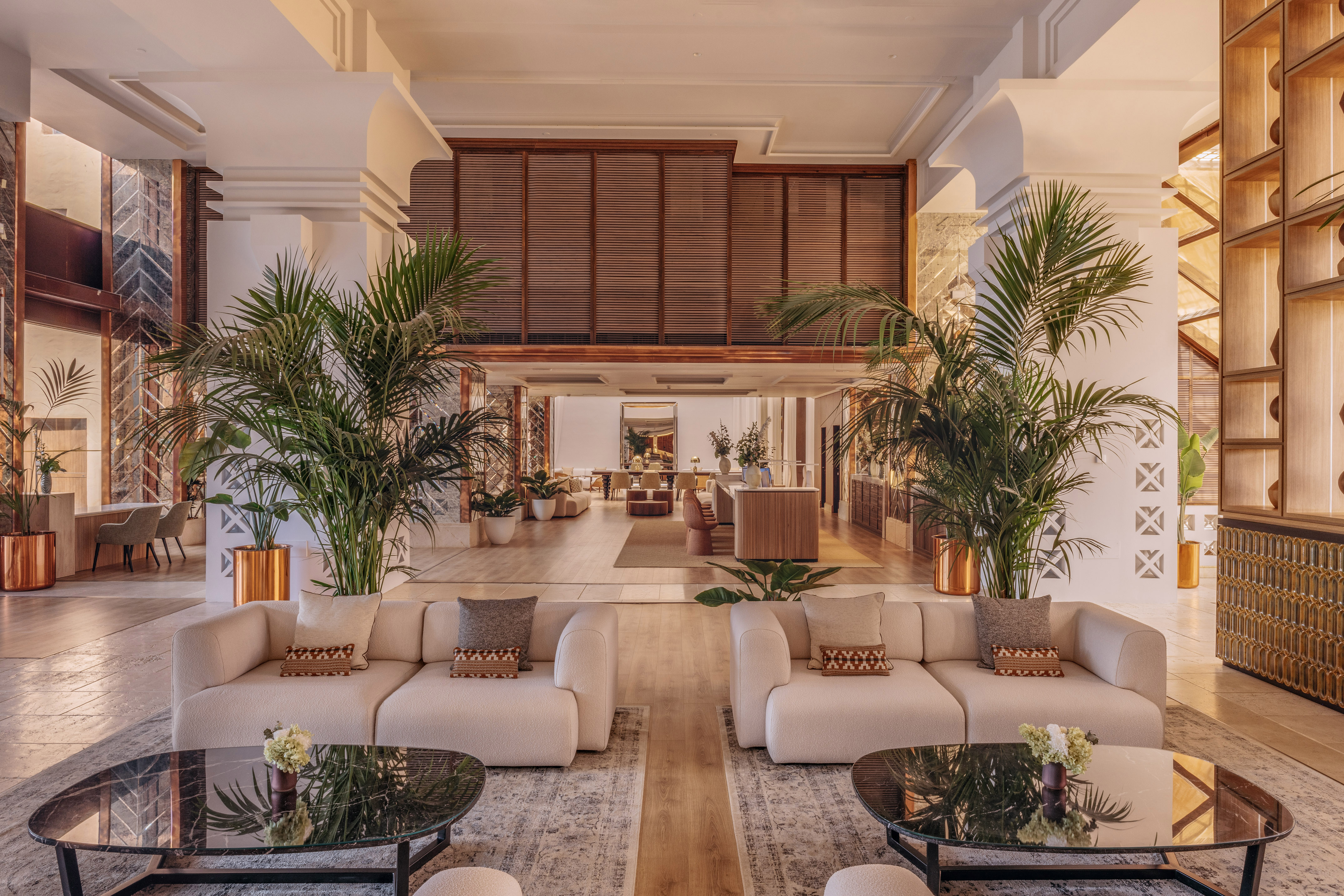 Modern hotel lobby with cream sofas, black marble tables, and lush palm plants.