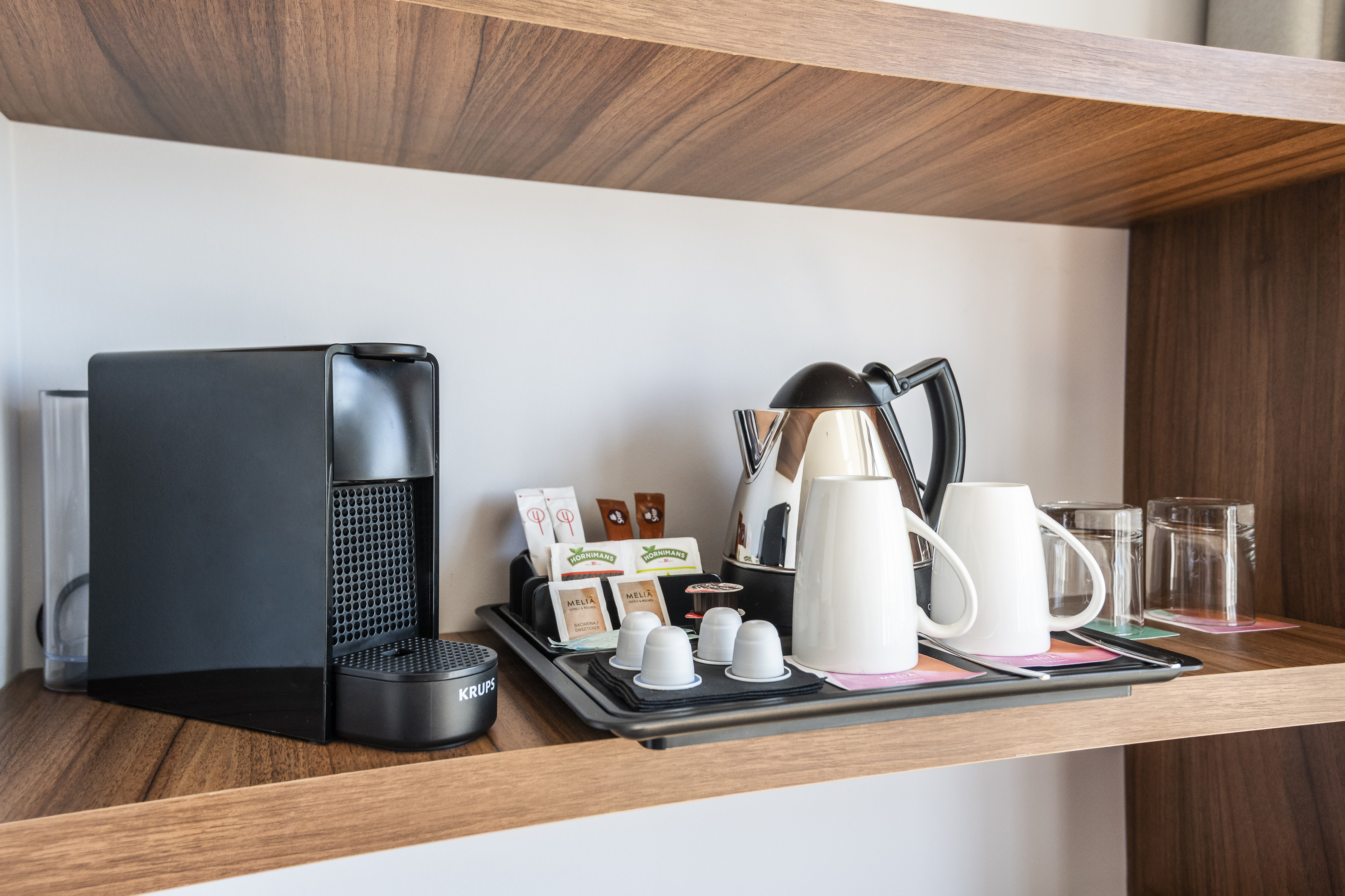 Hotel coffee station with Nespresso machine, kettle, mugs, and tea.