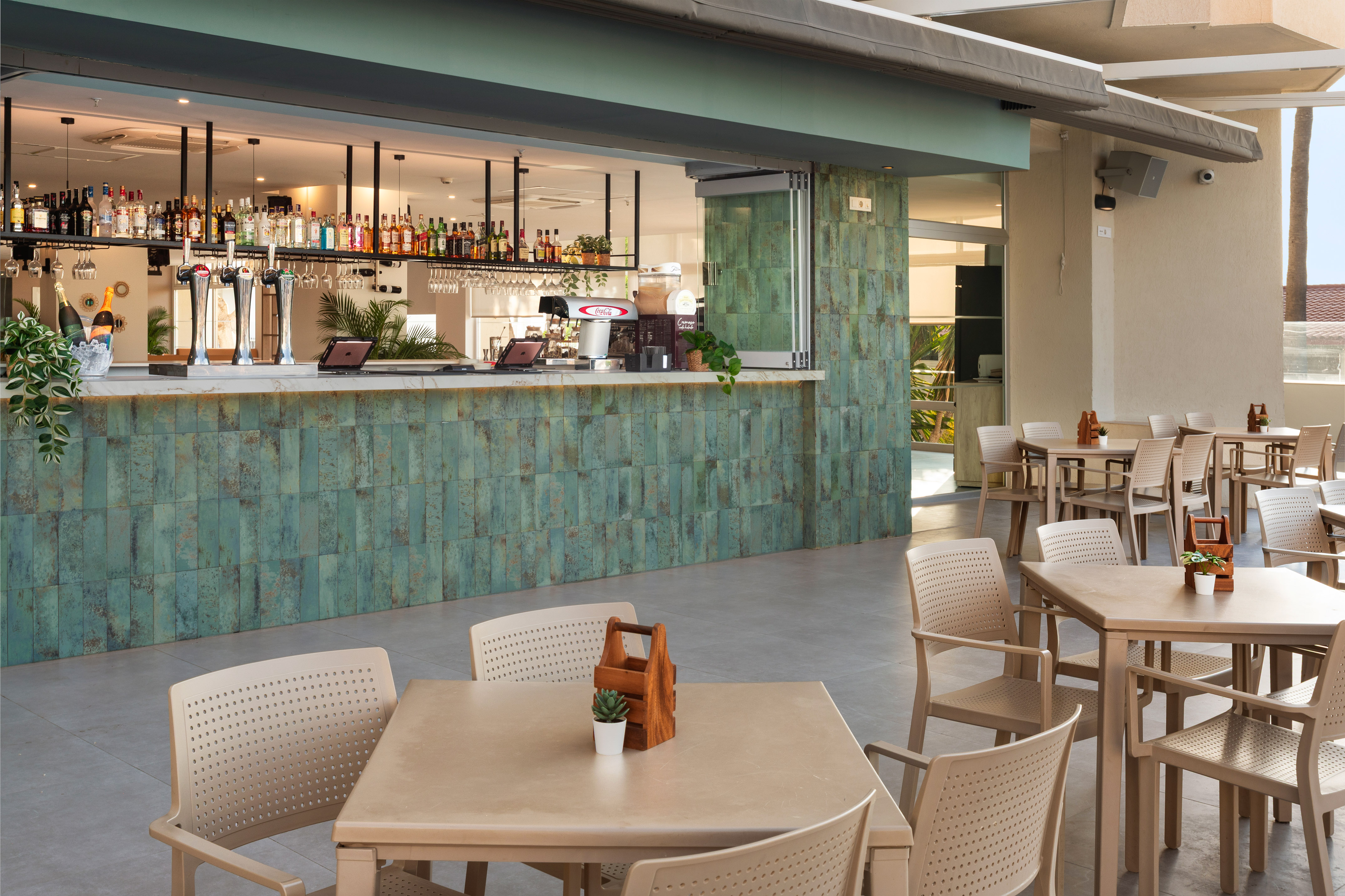 Outdoor bar area with green tiled counter, bottles, and multiple patio dining tables.
