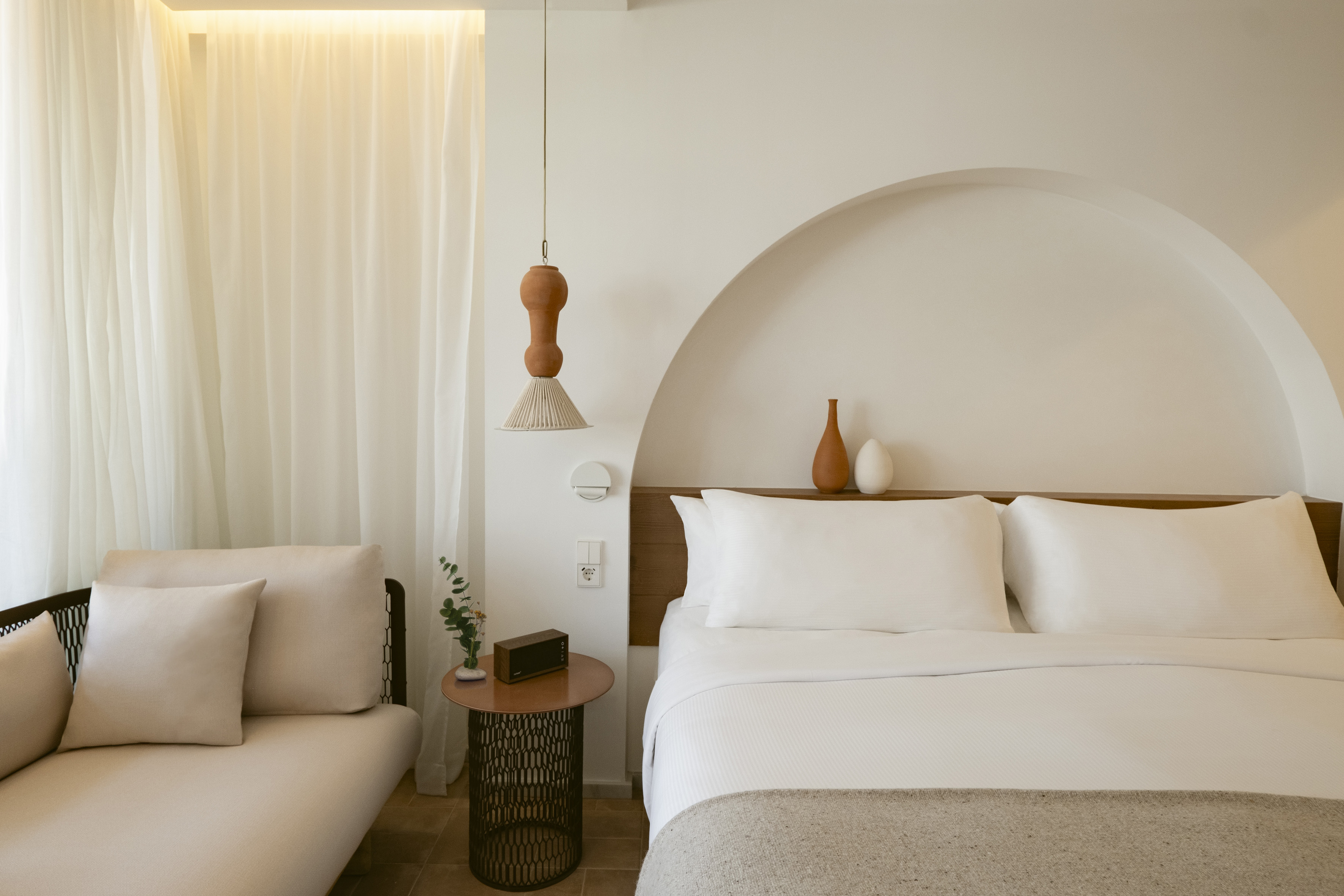 Modern hotel room with white bed, arched alcove, and terracotta pendant light.