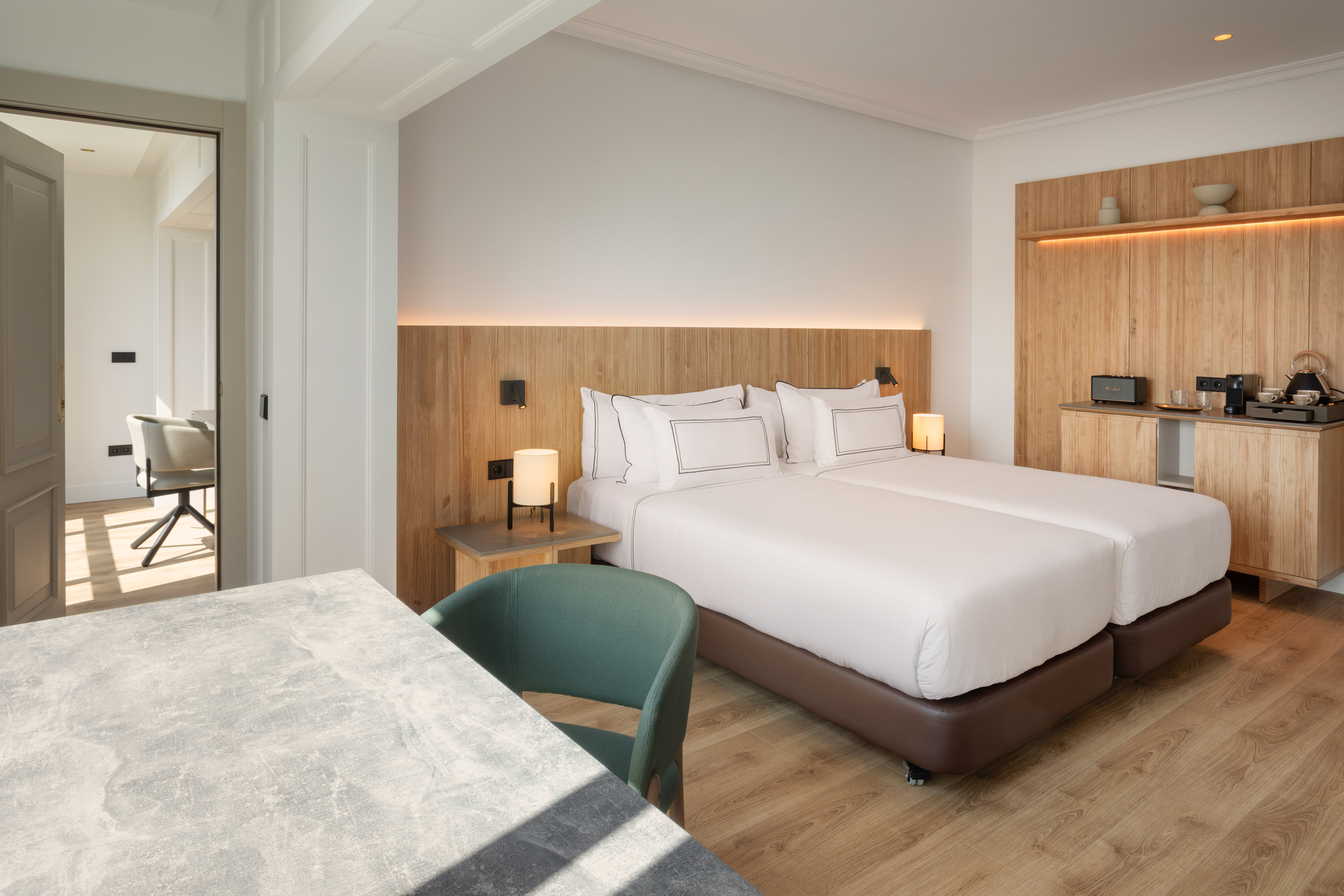 Modern hotel suite with twin beds, wooden headboard, and desk workspace.