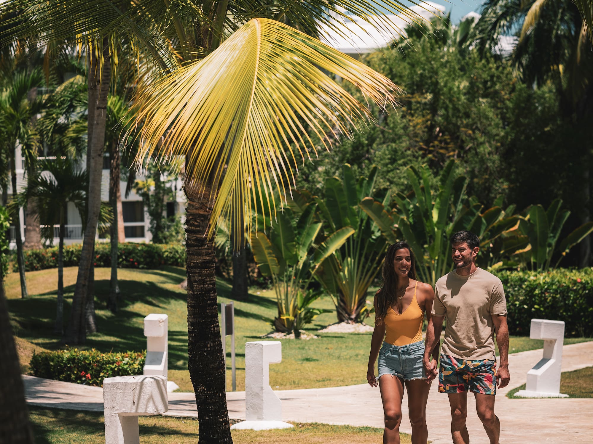 a man and woman walking on a sidewalk under a palm tree