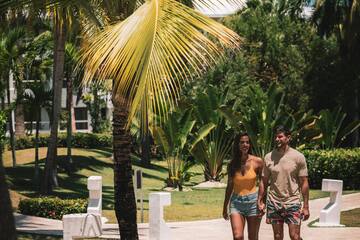 a man and woman walking on a sidewalk under a palm tree