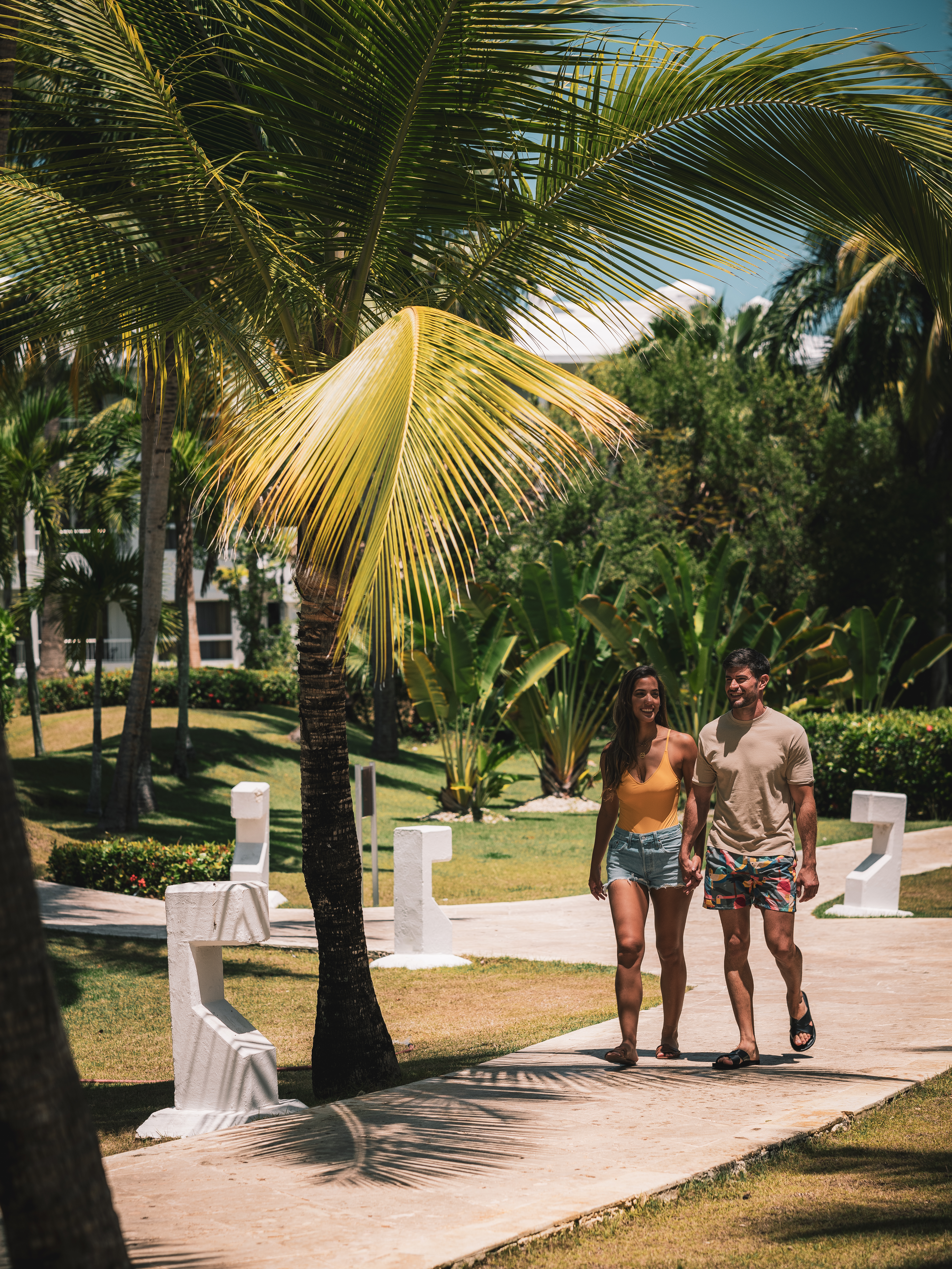 a man and woman walking on a sidewalk under a palm tree
