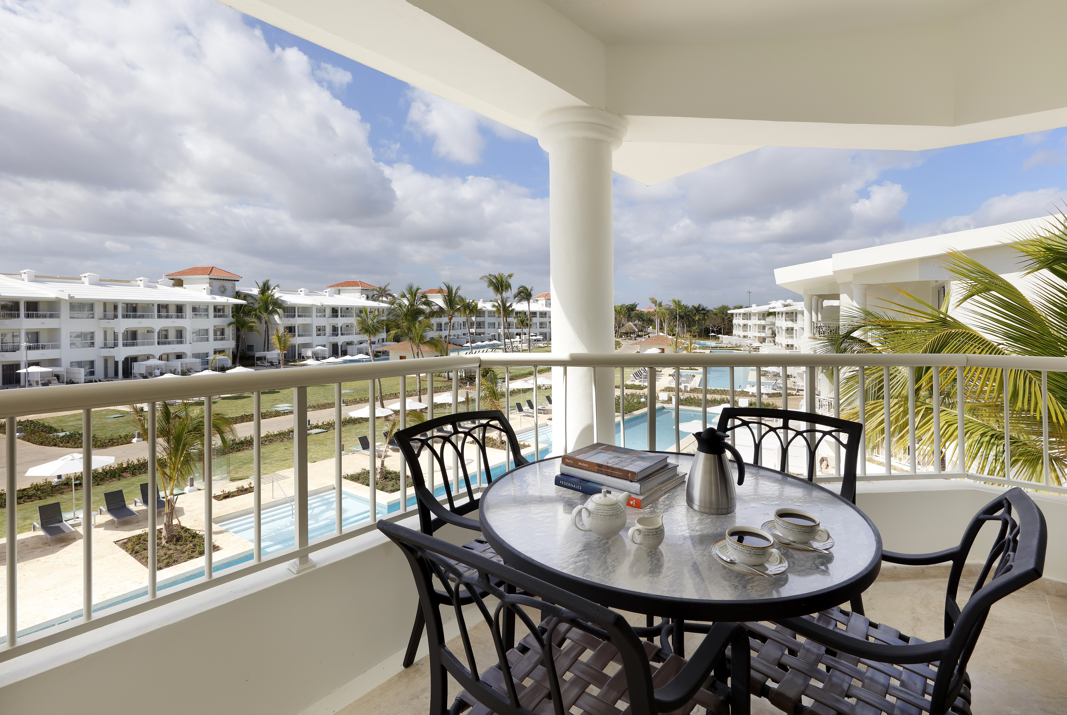 Hotel balcony with coffee, books, overlooking resort pools and palm trees.