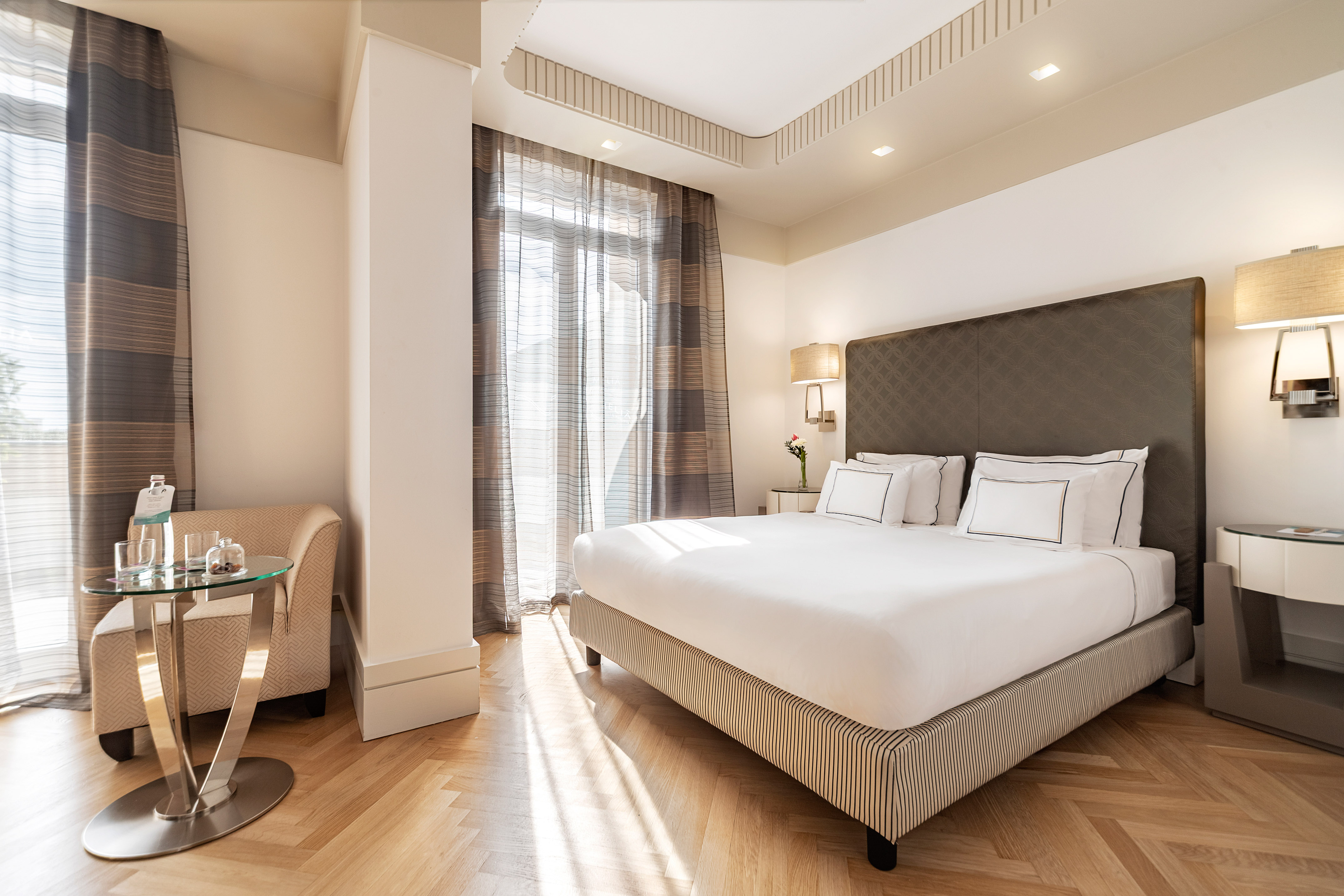 Sunny luxury hotel room with king bed and herringbone wood floor.