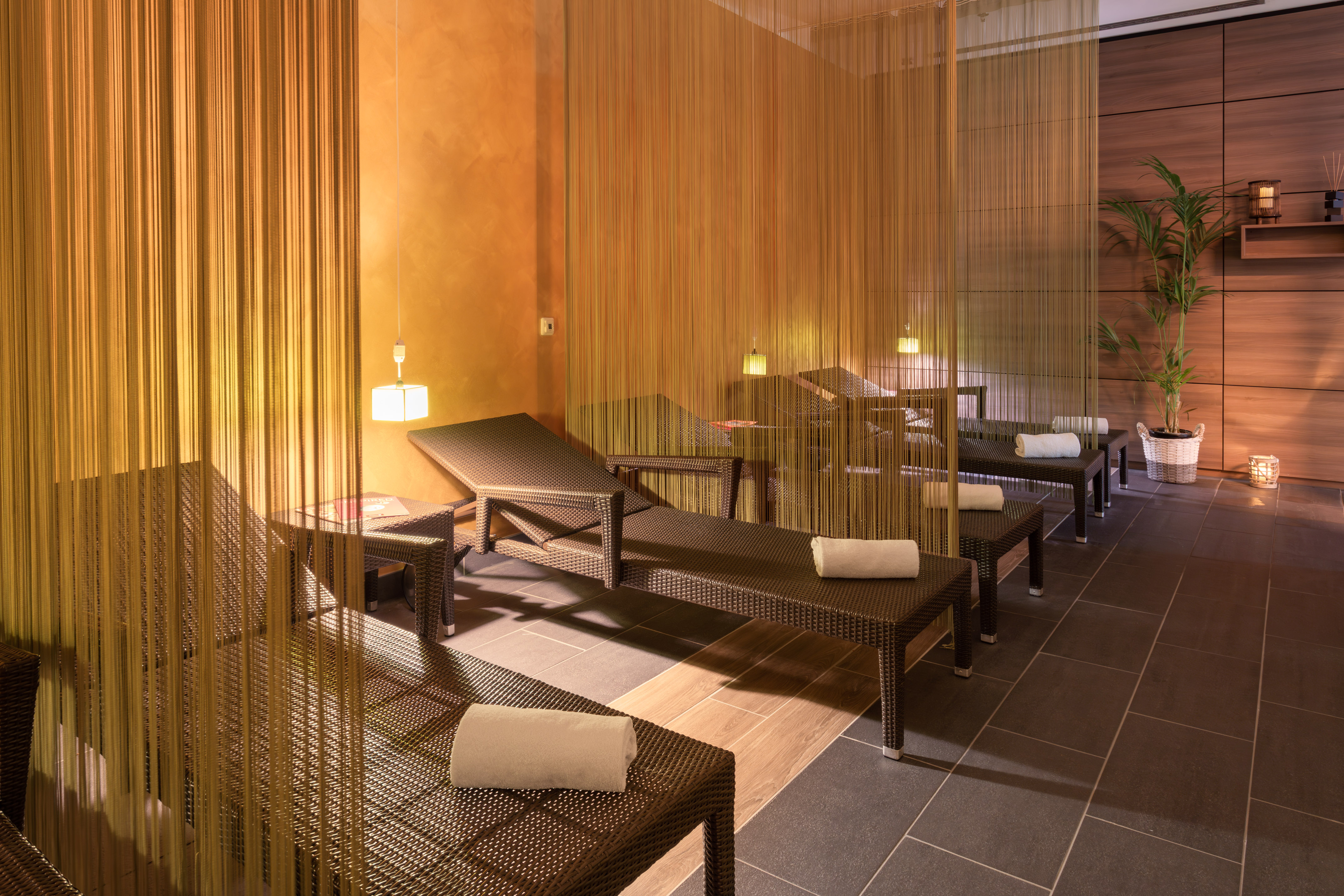Cozy spa relaxation room with wicker lounge chairs, soft lighting, and string curtains.