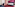 Magenta and pink hotel room with blue bed, red carpet, desk, and sofa.