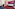 Magenta and pink hotel room with blue bed, red carpet, desk, and sofa.