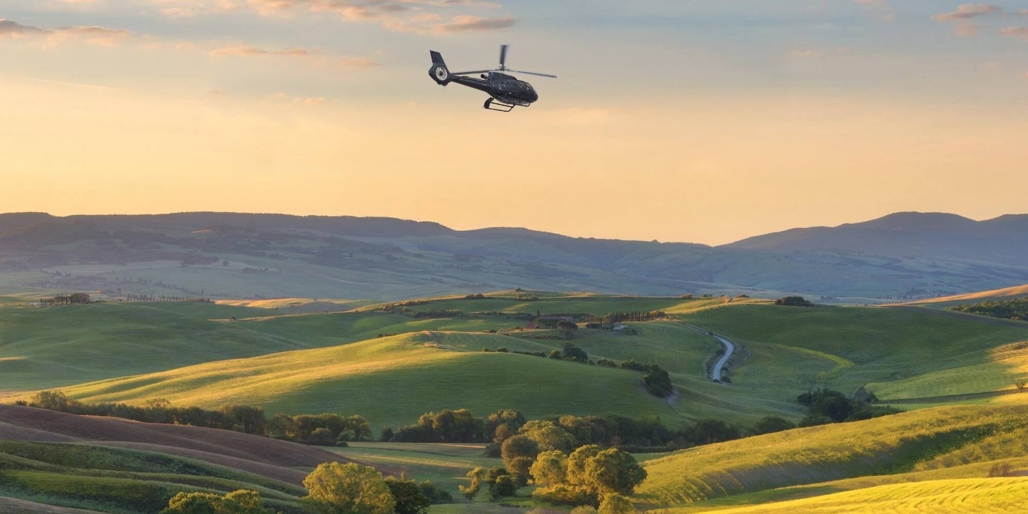 Helicopter flying above green rolling hills, golden sunset. Tuscany landscape.