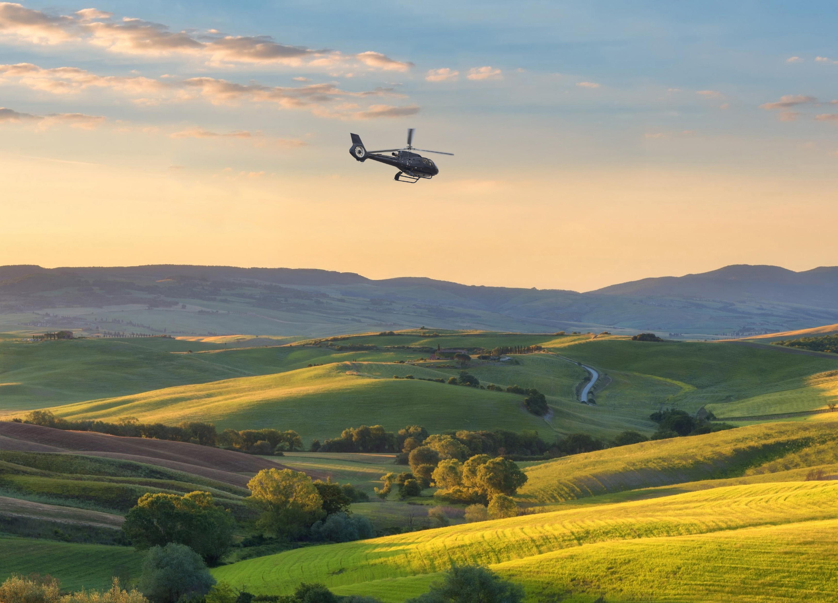 Helicopter flying above green rolling hills, golden sunset. Tuscany landscape.