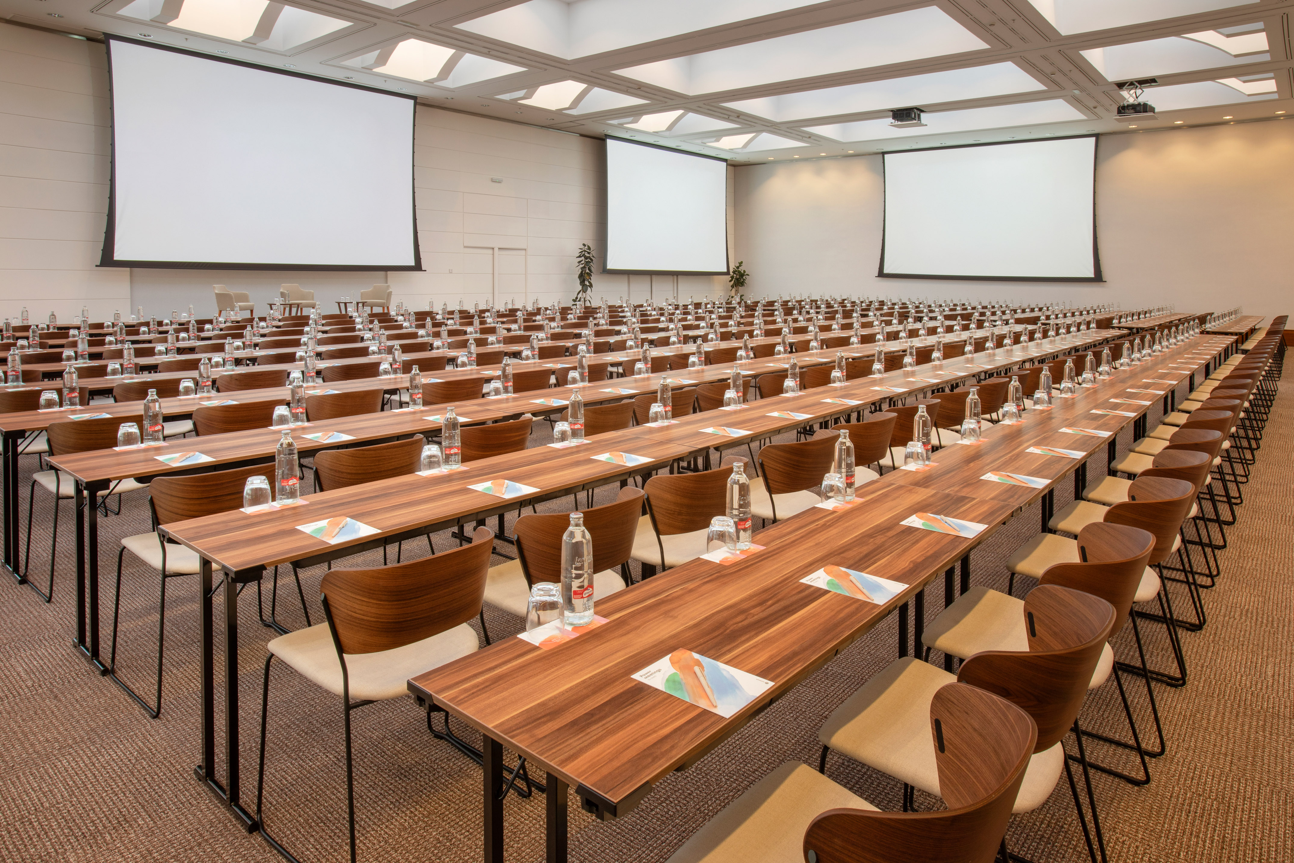 Conference room for events: rows of tables, chairs, and multiple projector screens.