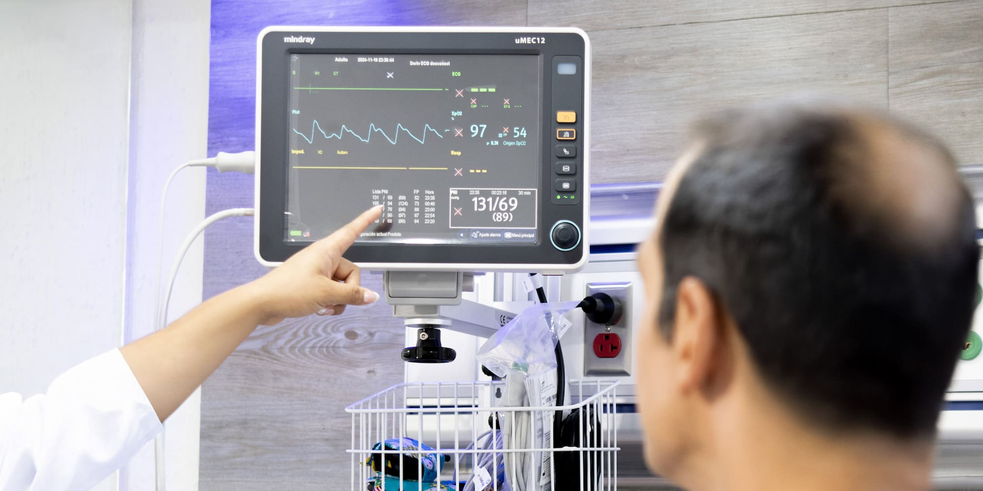 Healthcare professional points at Mindray patient monitor displaying vital signs.