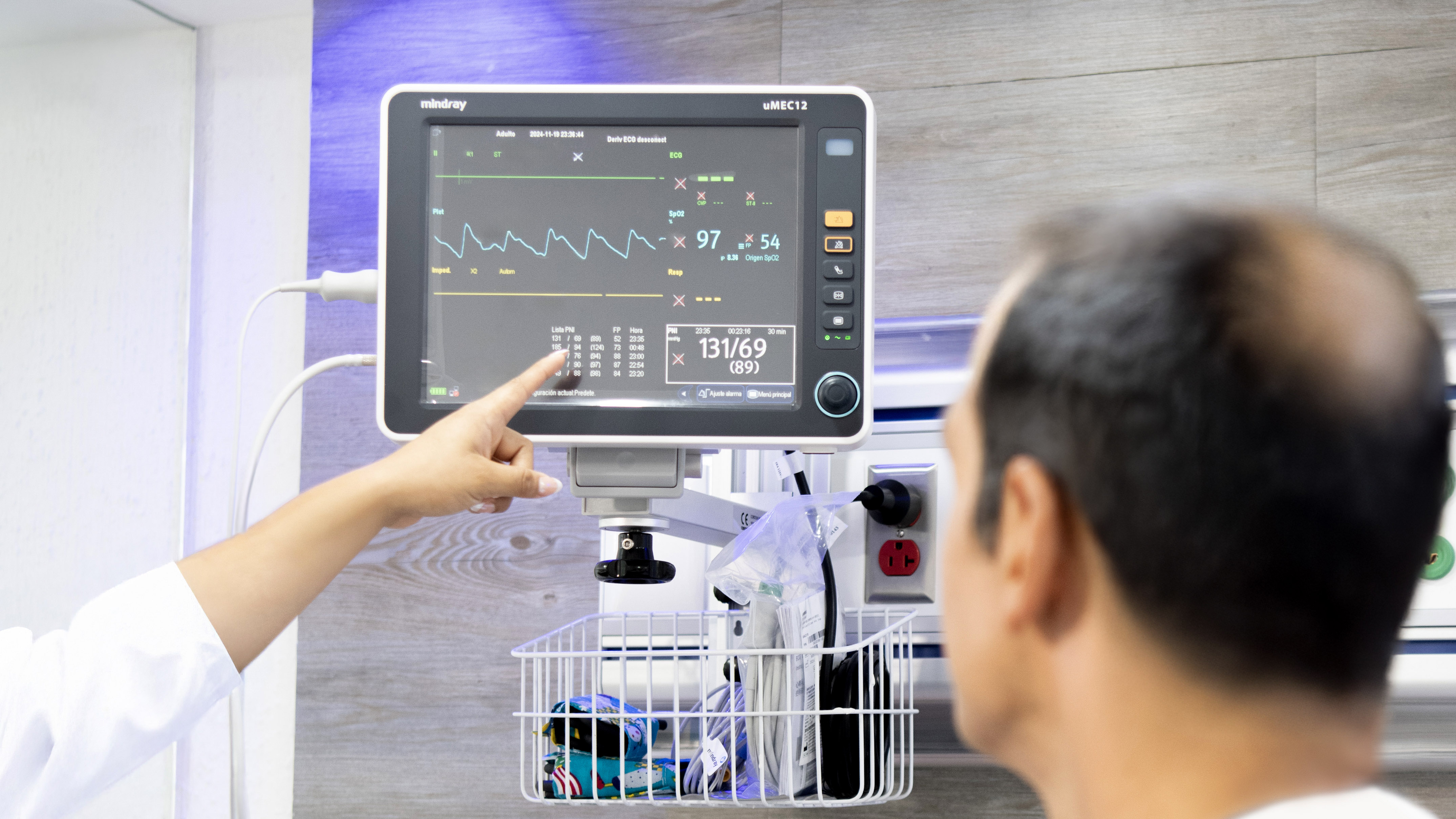 Healthcare professional points at Mindray patient monitor displaying vital signs.